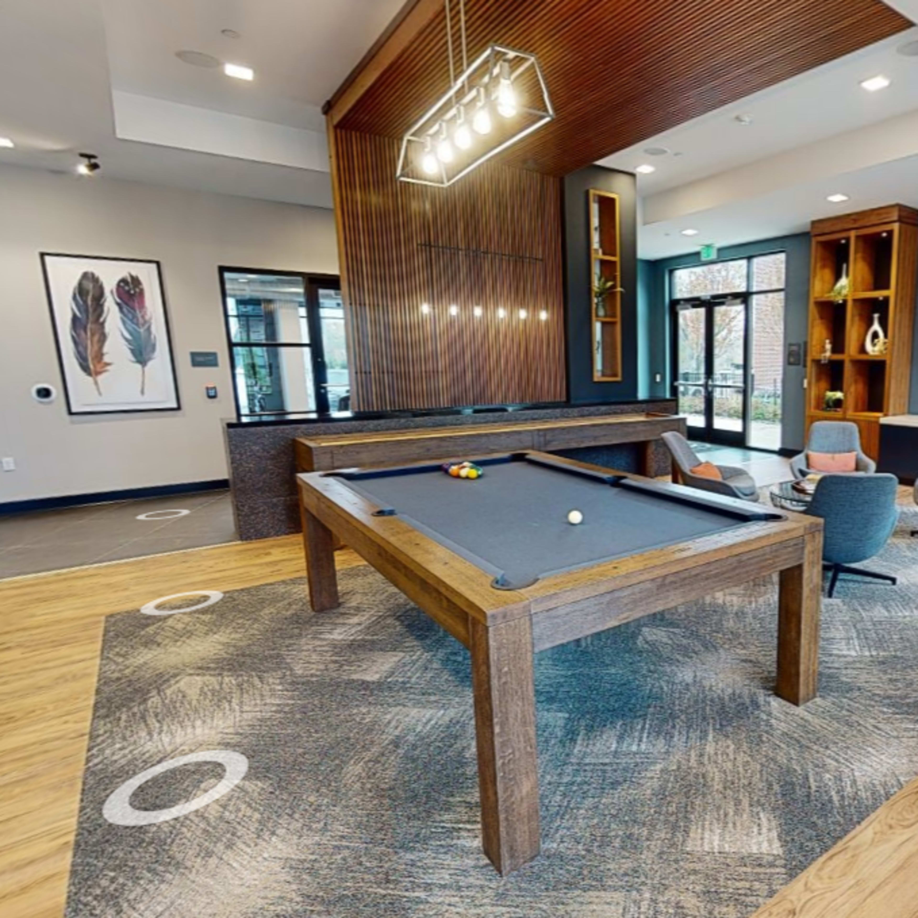 A modern game room featuring a billiards table, seating areas, and large windows.
