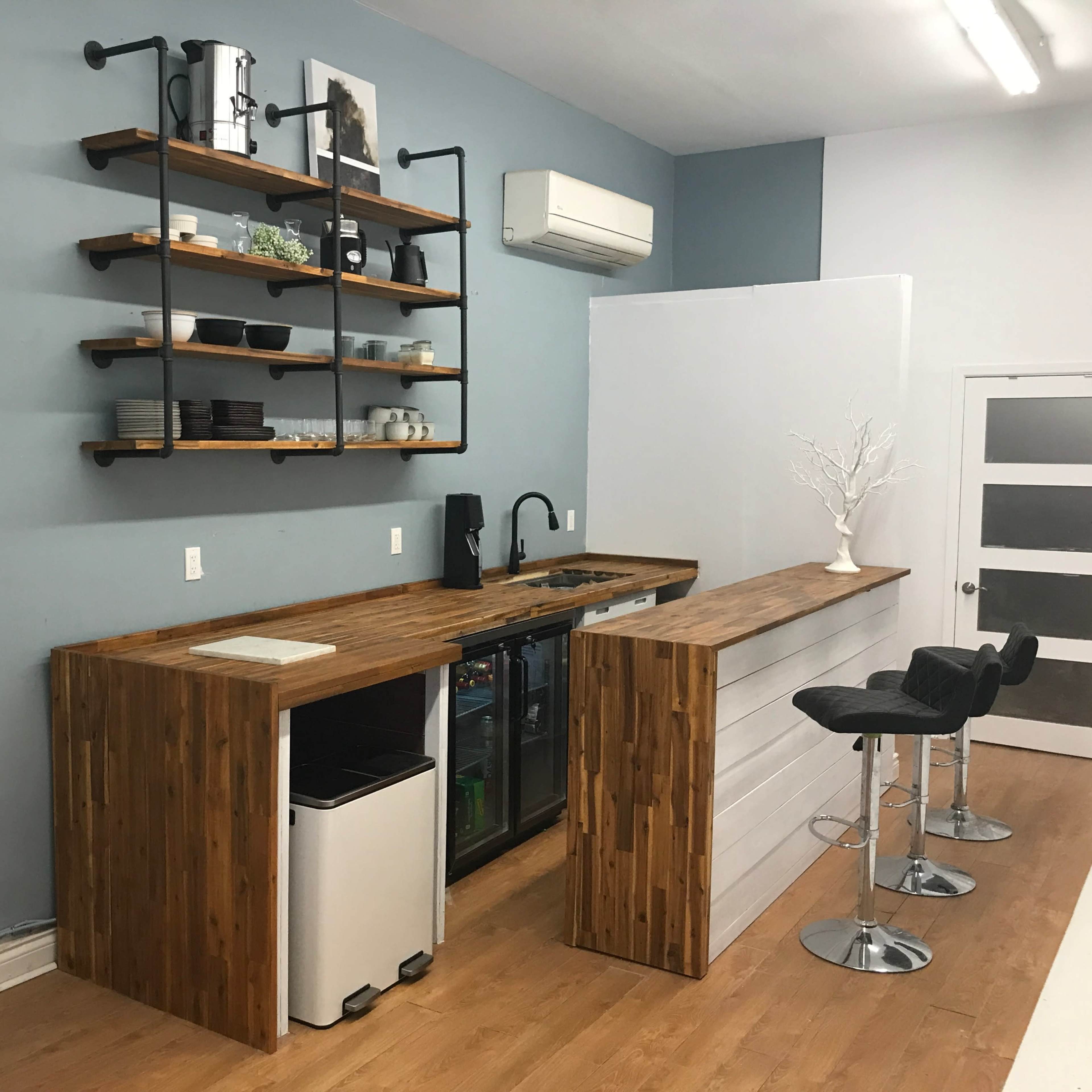 A modern kitchen with a wooden countertop, a small sink, and shelves displaying kitchen items, set against a blue wall.