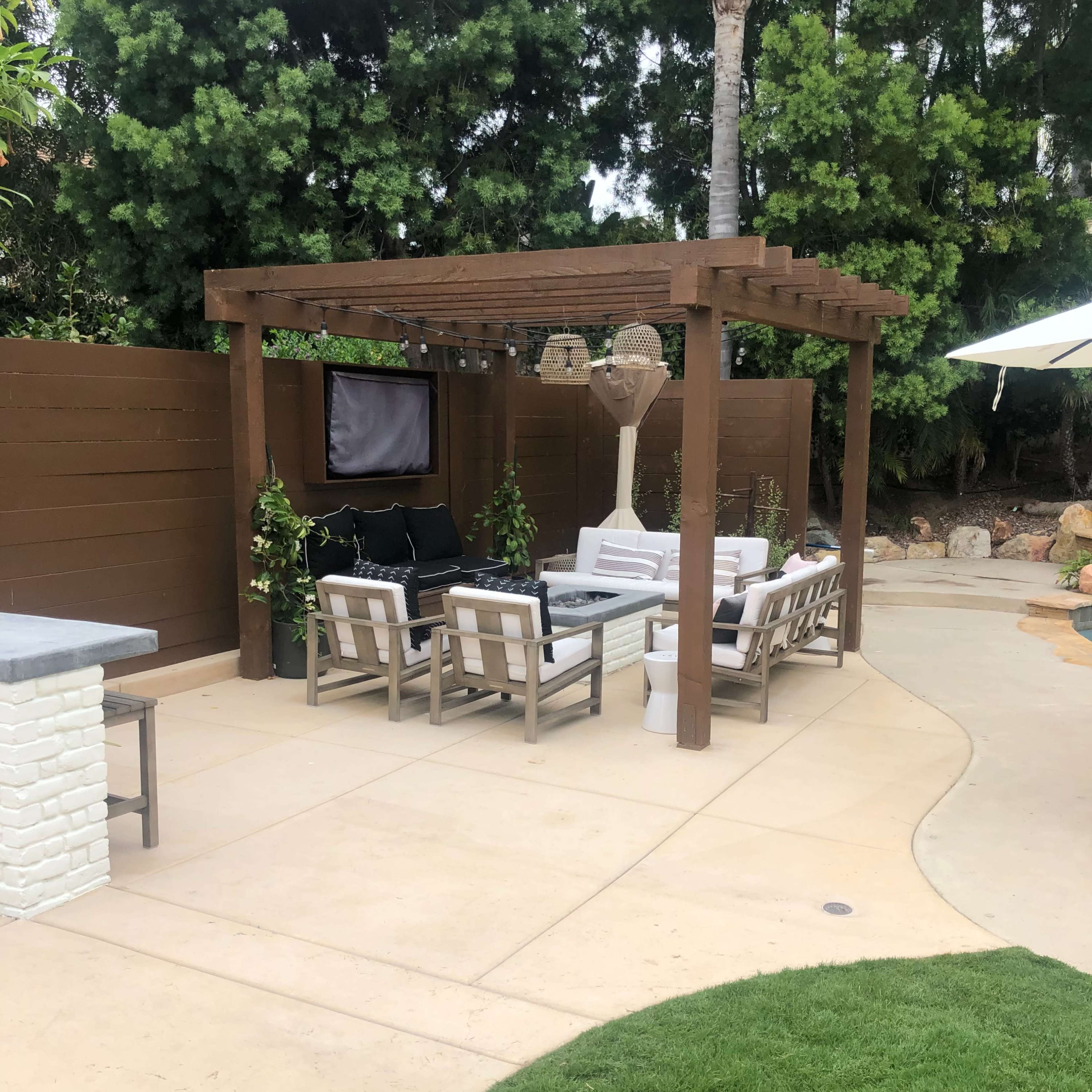 A shaded outdoor seating area with a pergola, featuring a mix of lounge furniture and surrounding greenery.