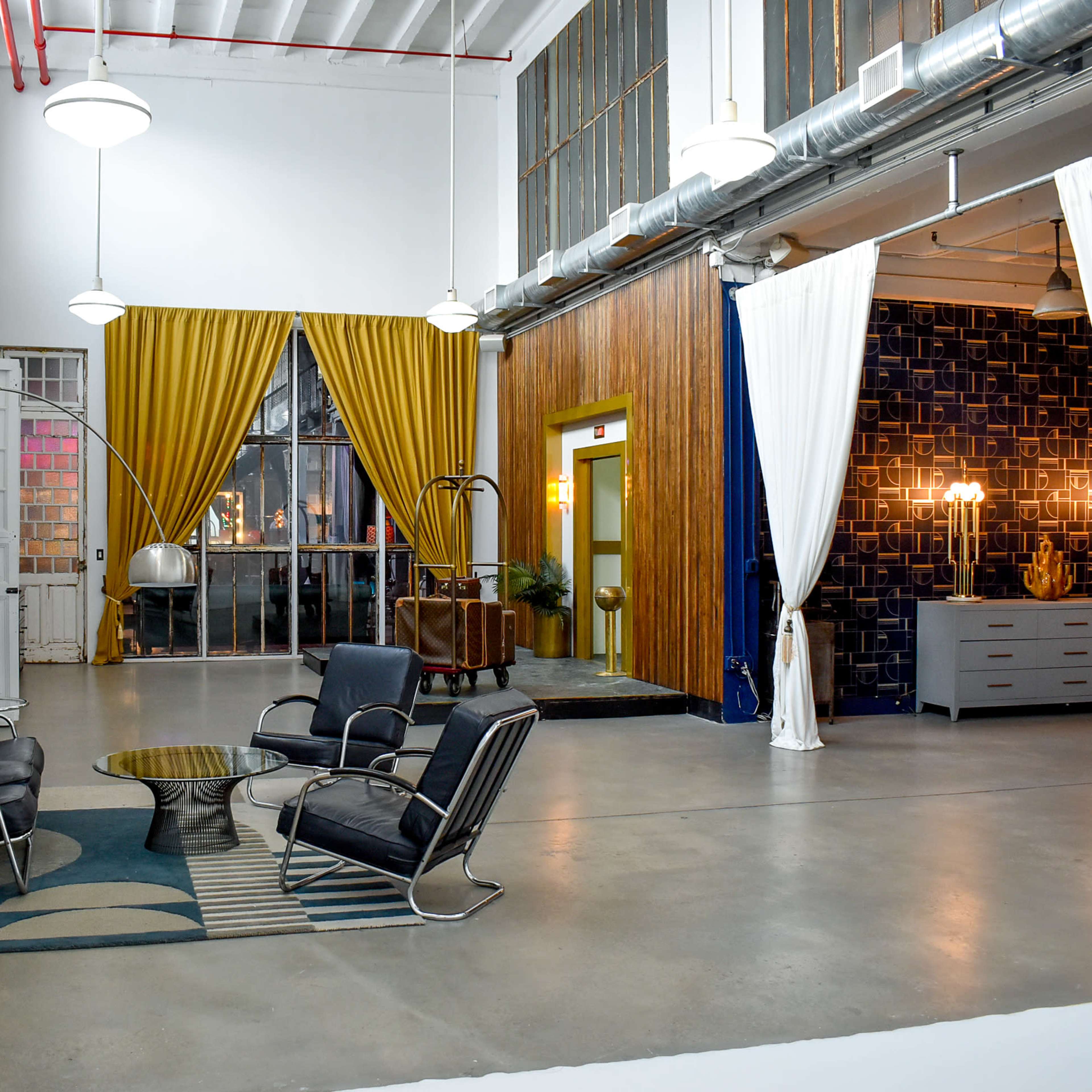 A spacious interior with modern furniture, featuring a seating area with black chairs and a round table, separated by decorative curtains and walls in various colors.
