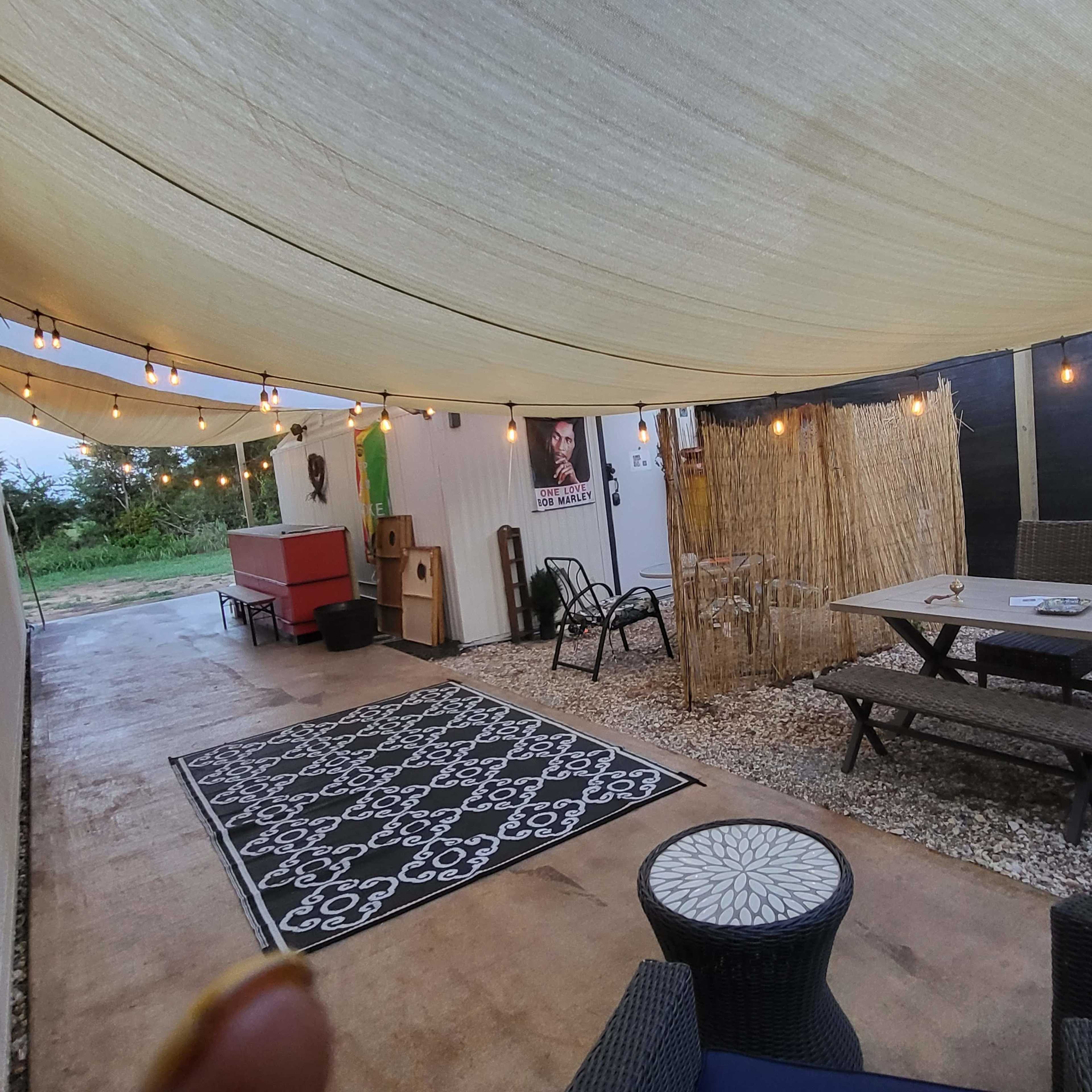 A covered outdoor patio area featuring a large table, chairs, decorative string lights, and a patterned rug.