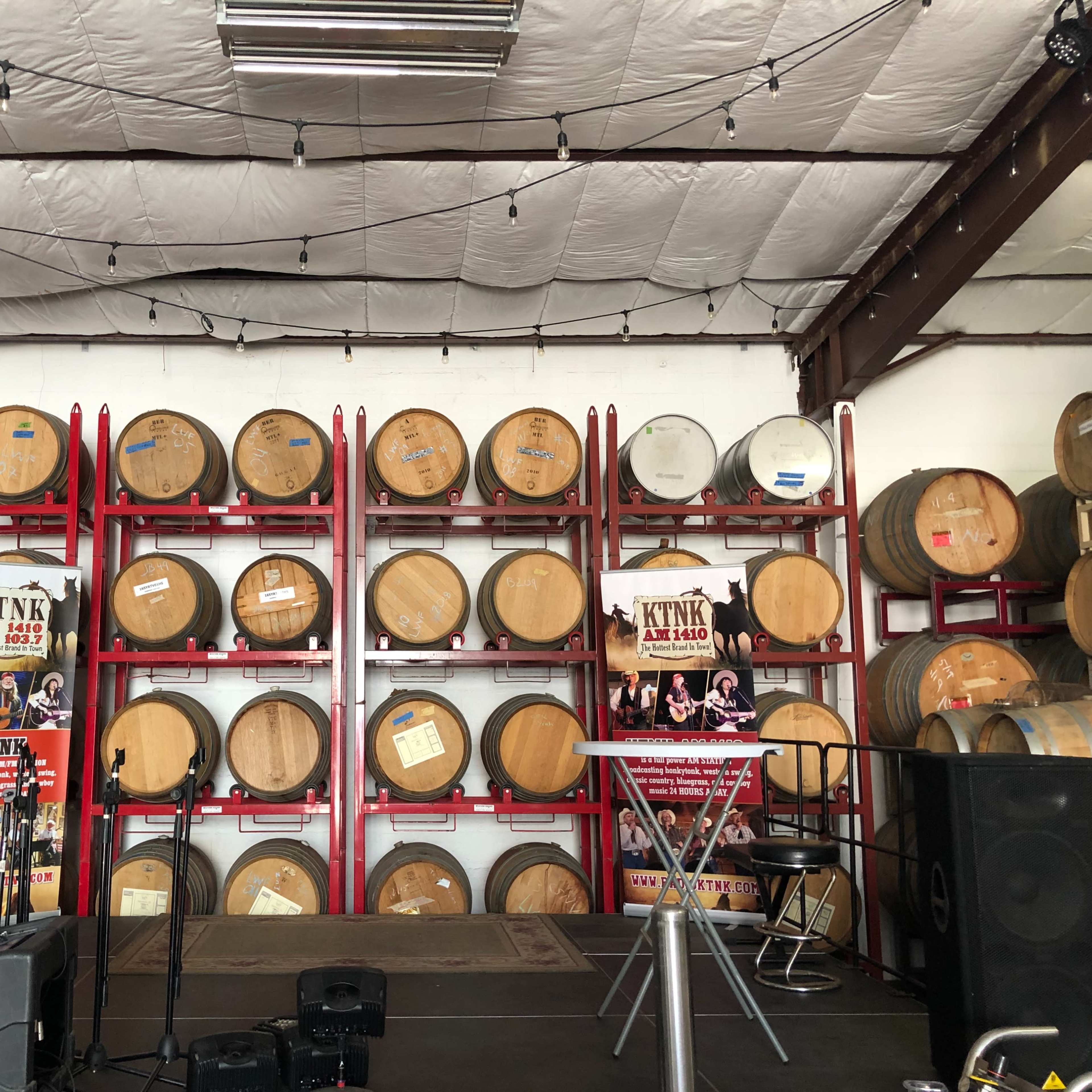 A staged area with wooden barrels stacked on red metal racks in a warehouse setting, accompanied by promotional posters.