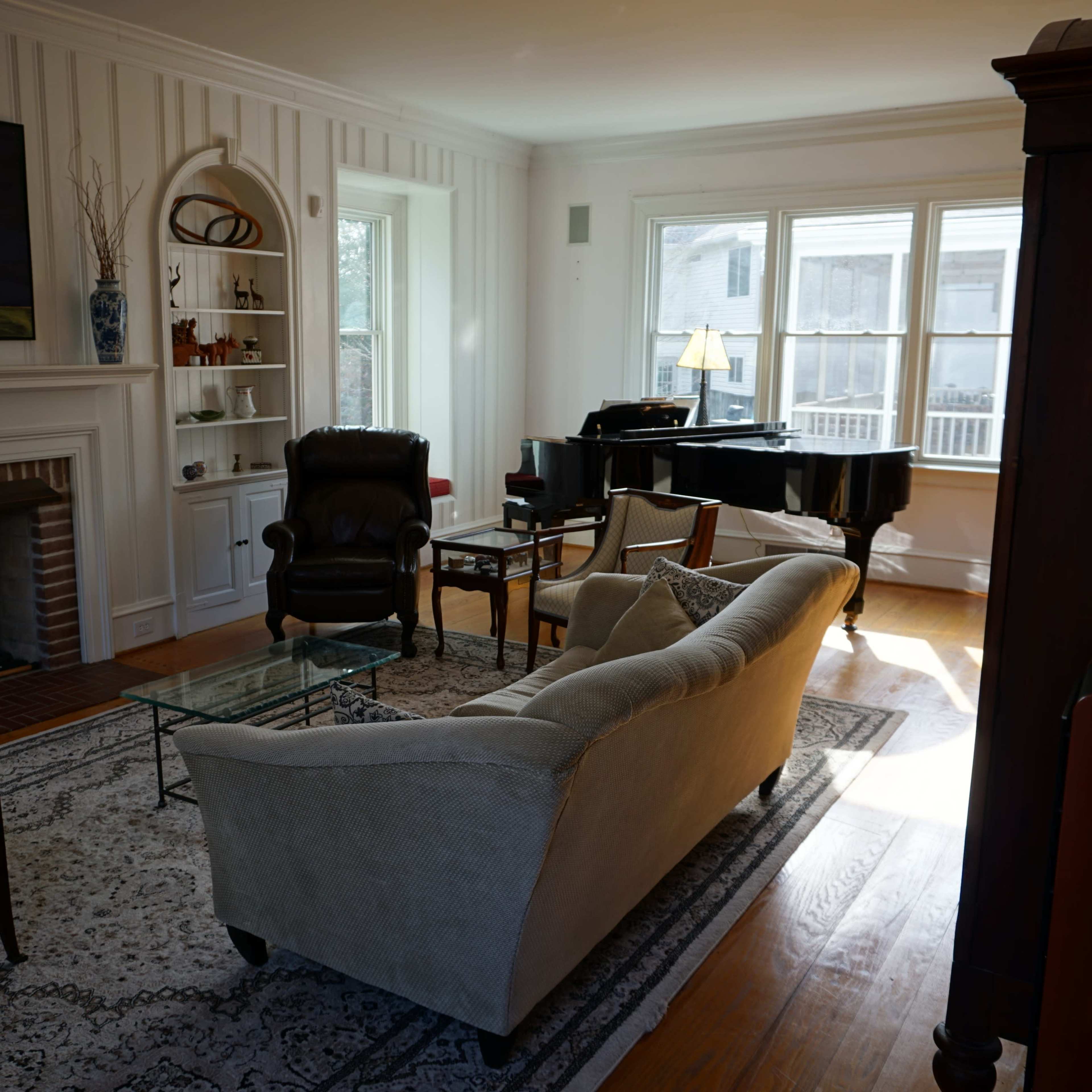 A cozy living room featuring a piano, a fireplace, and a mix of comfortable seating arranged around a glass coffee table.