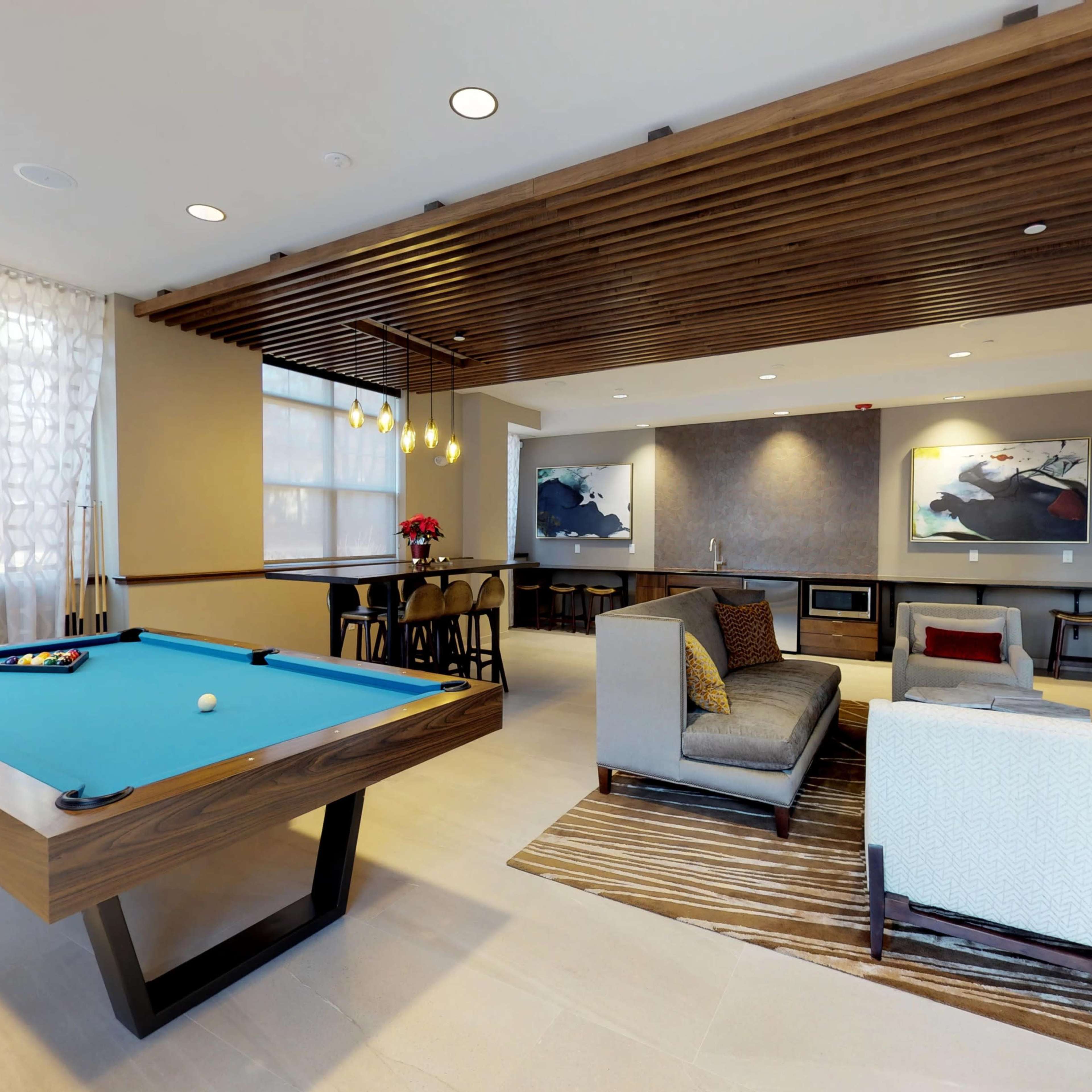 A modern lounge area featuring a billiards table, a comfortable seating arrangement, a fireplace, and artwork on the walls.