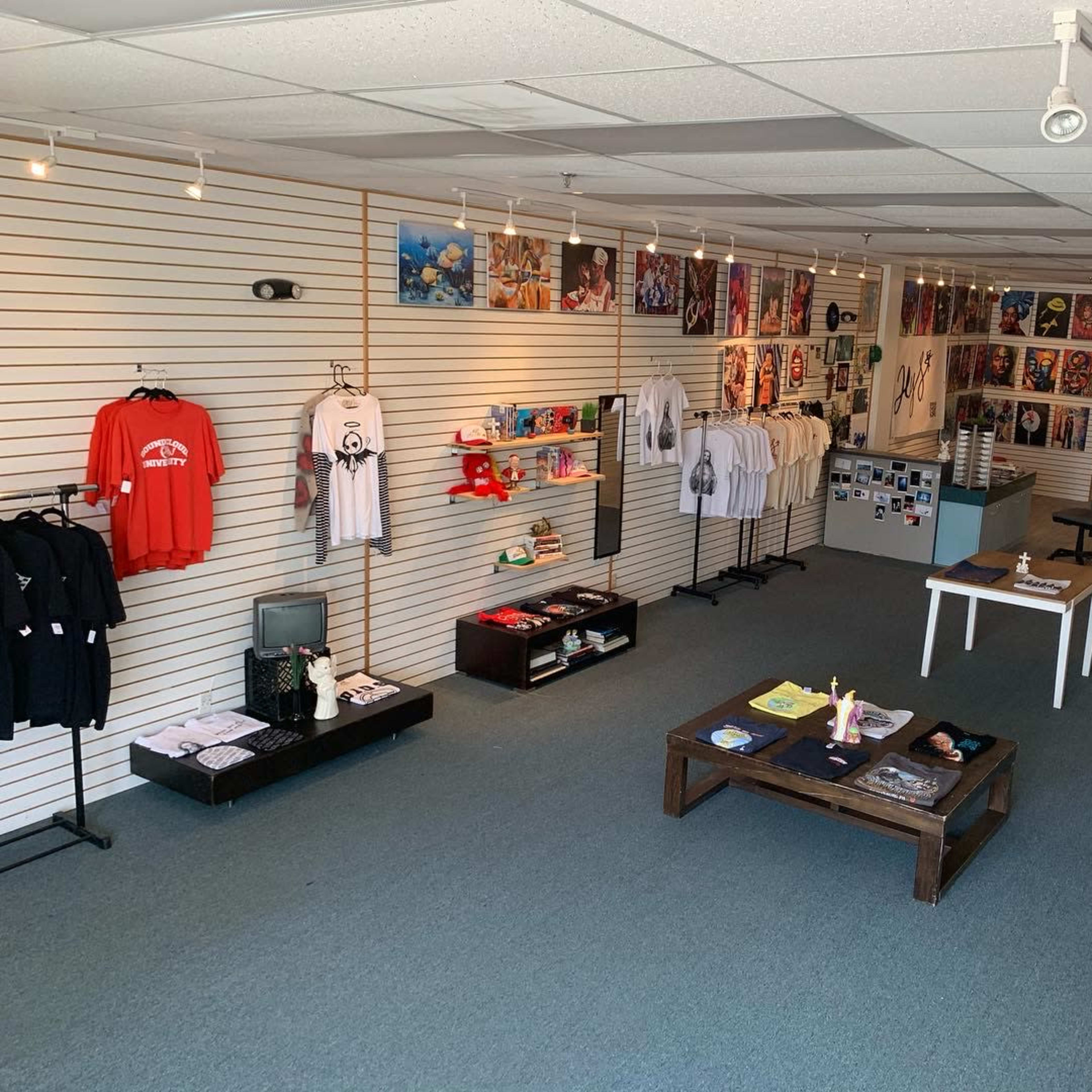 An art and merchandise store with clothing displayed on racks and various artworks hanging on the walls.