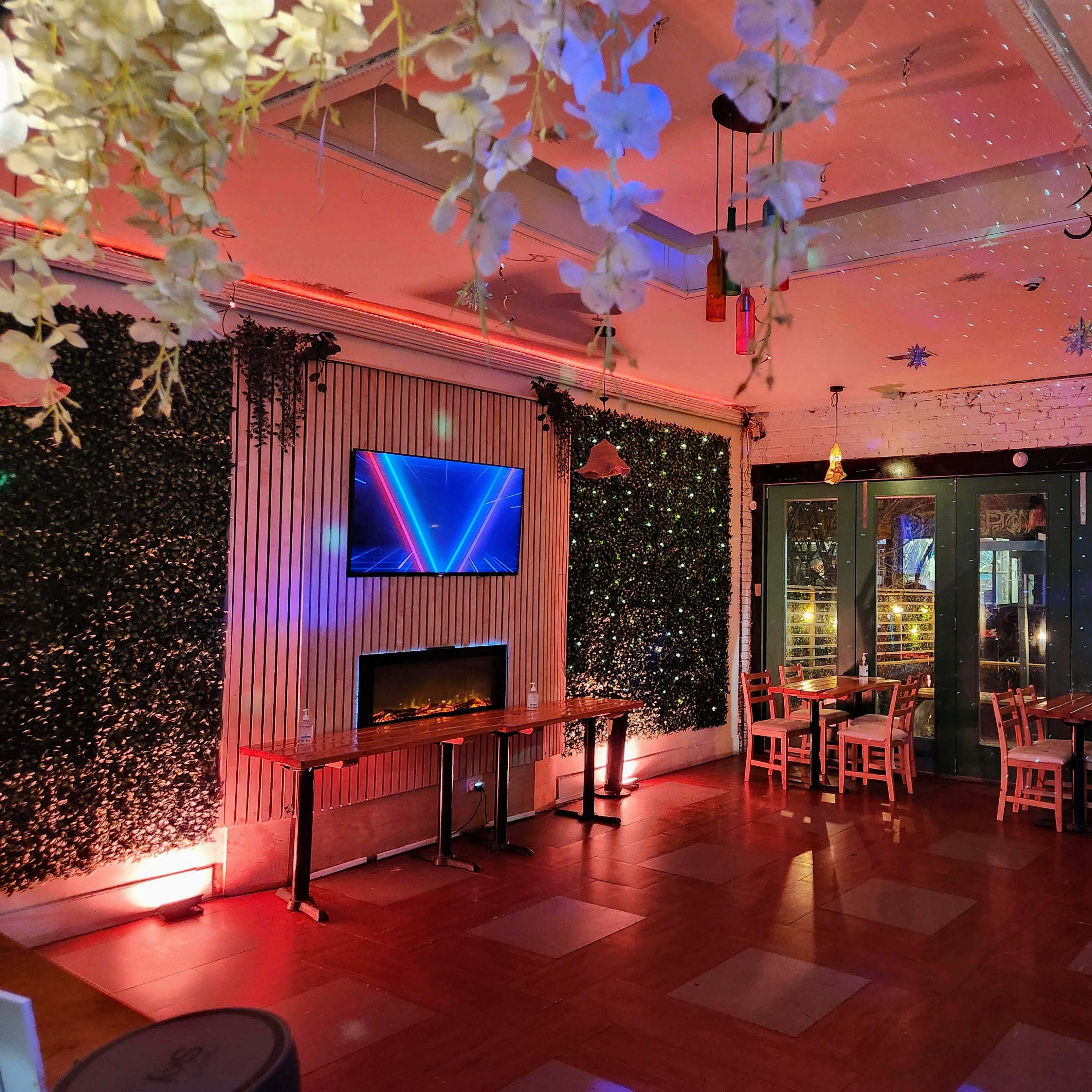 An indoor restaurant with a cozy setup, featuring a television on one wall, an electric fireplace, and tables arranged near large glass doors leading outside.