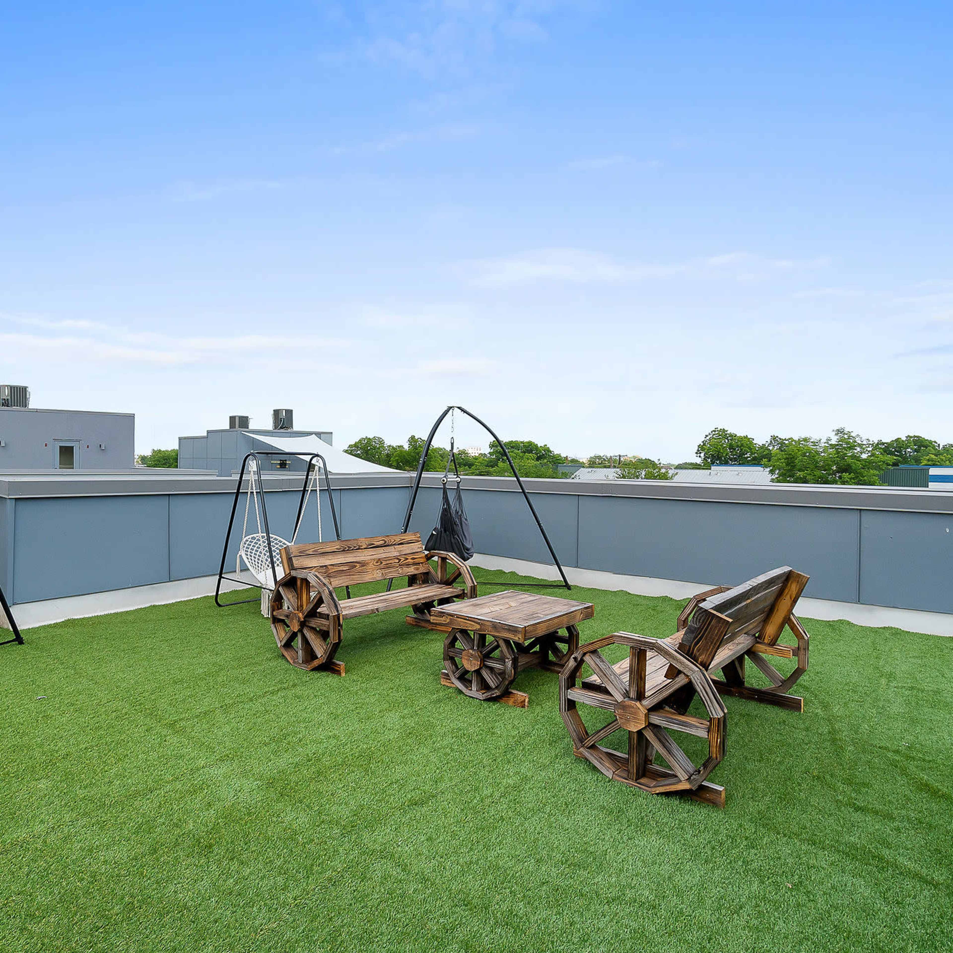 A rooftop terrace features artificial grass, wooden furniture, and two swings suspended from black frames.