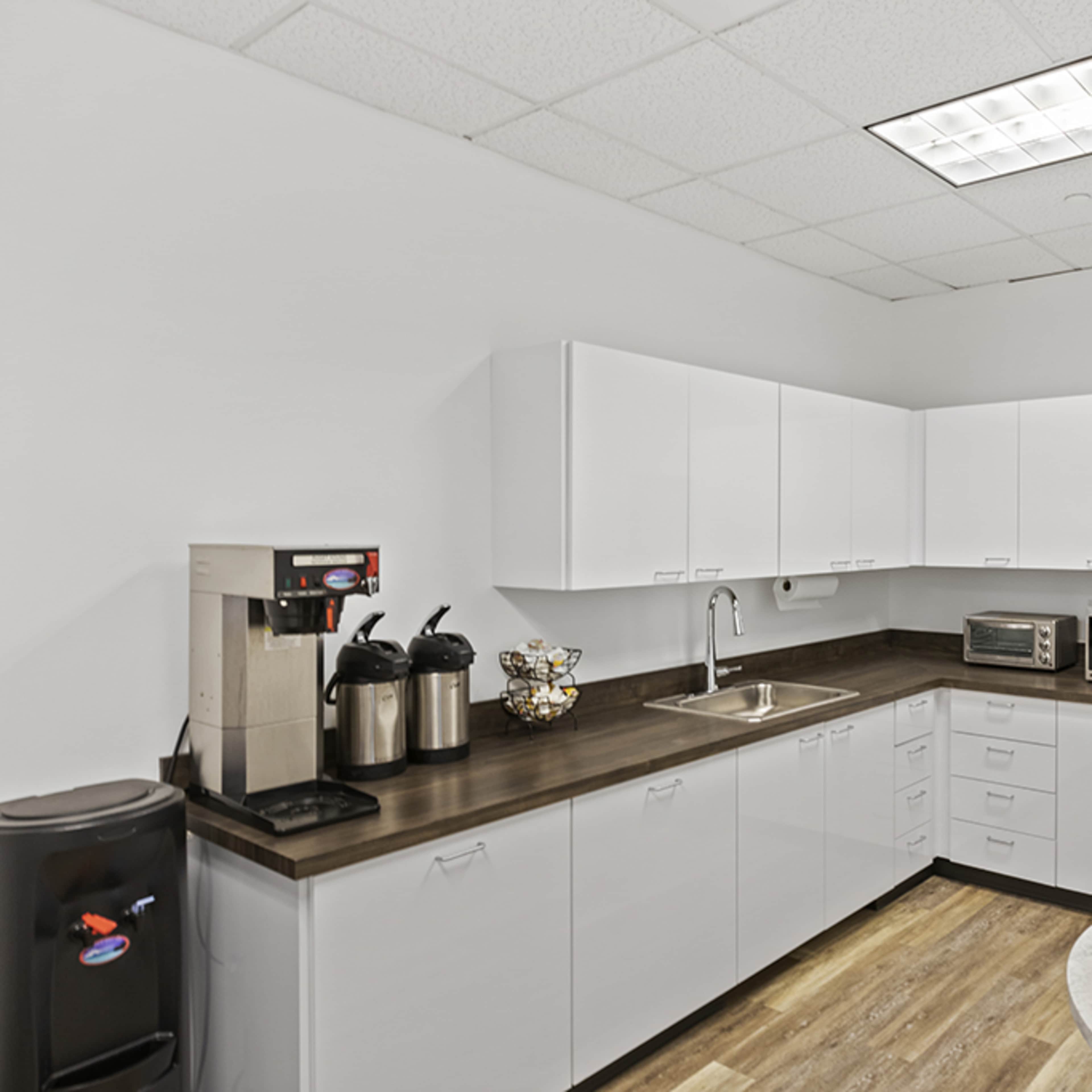 A modern kitchen equipped with white cabinets, a stainless steel refrigerator, and appliances including a coffee maker and microwave.