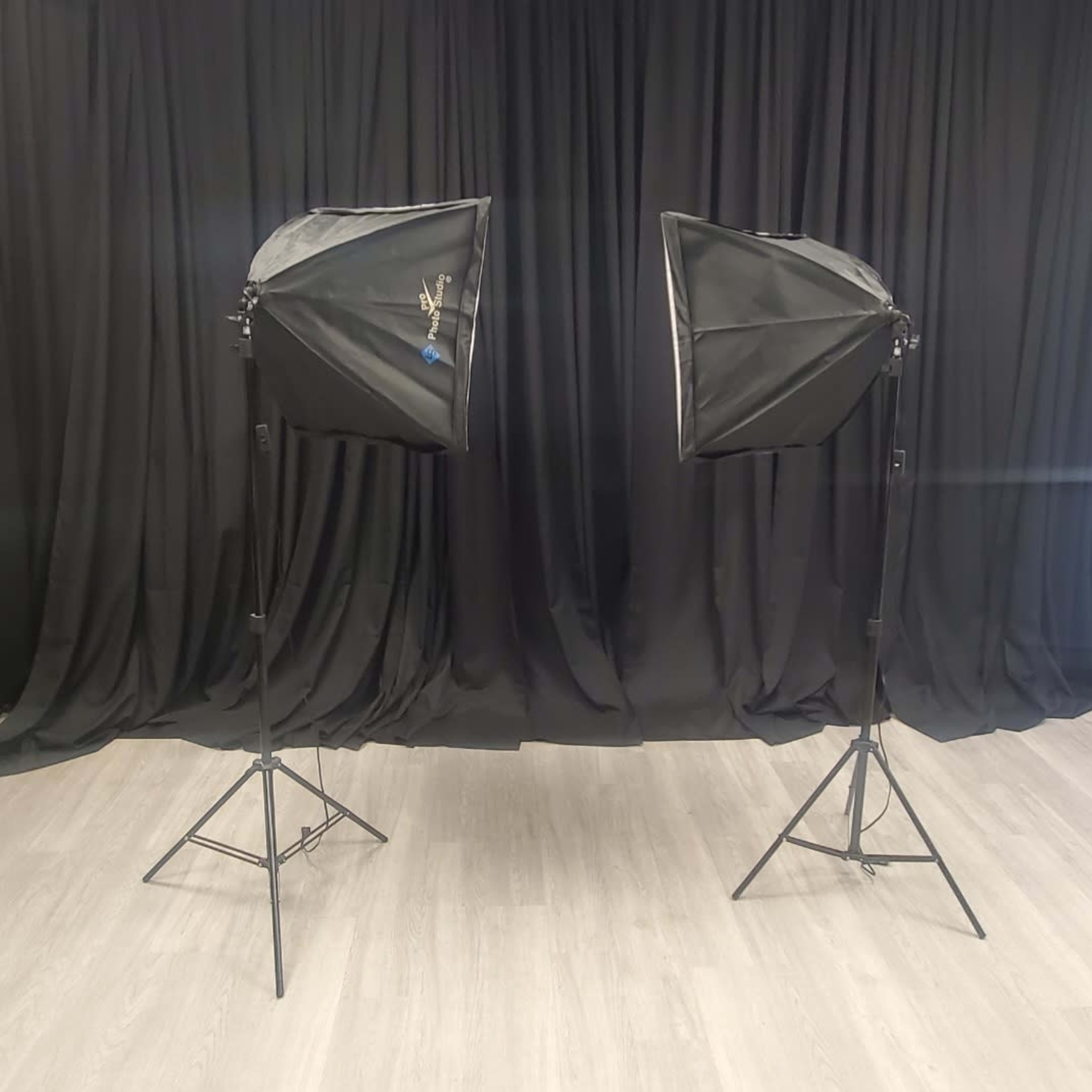 Two softbox lights on adjustable stands facing each other against a backdrop of black fabric.