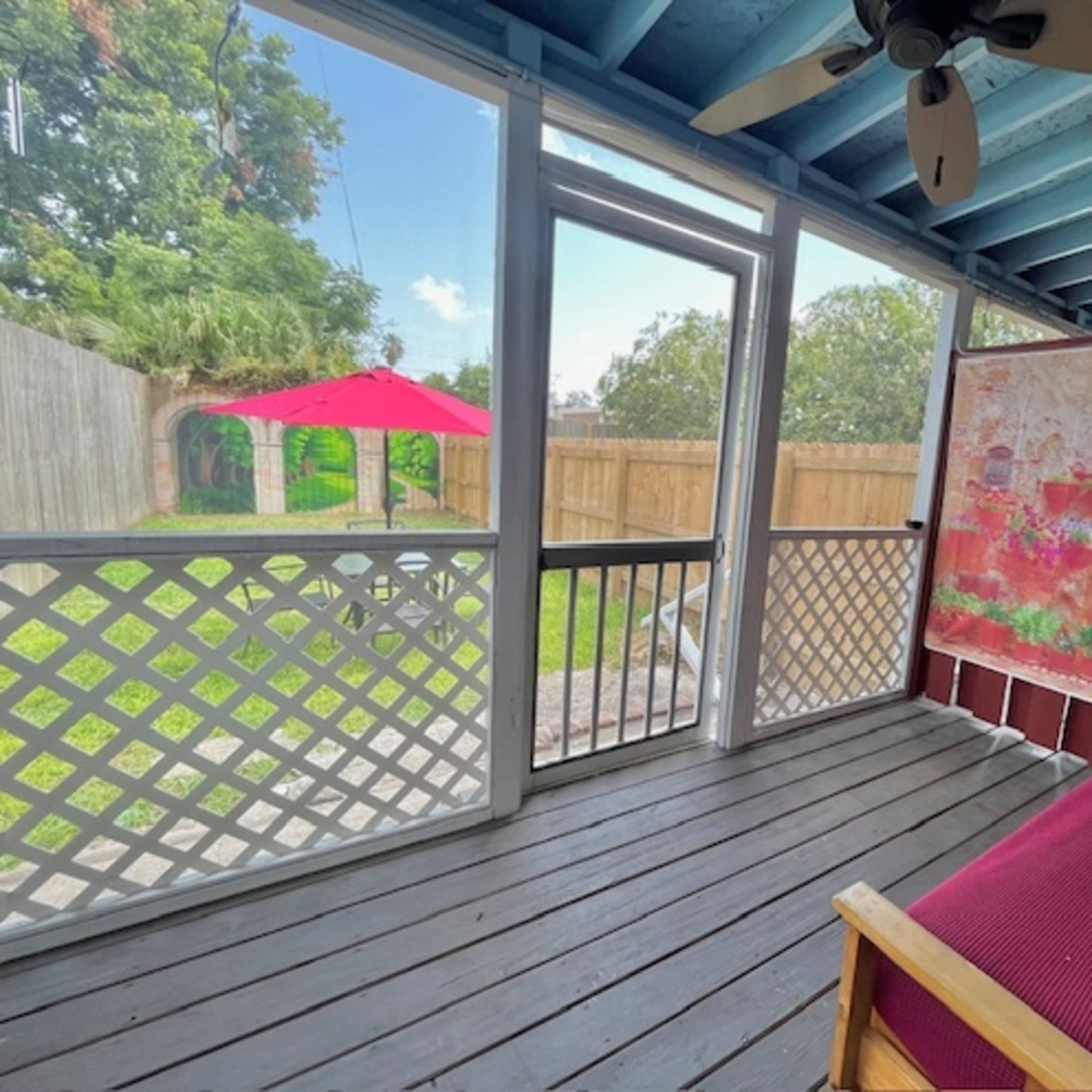 A screened porch with a view of a backyard featuring a red umbrella and a green lawn.