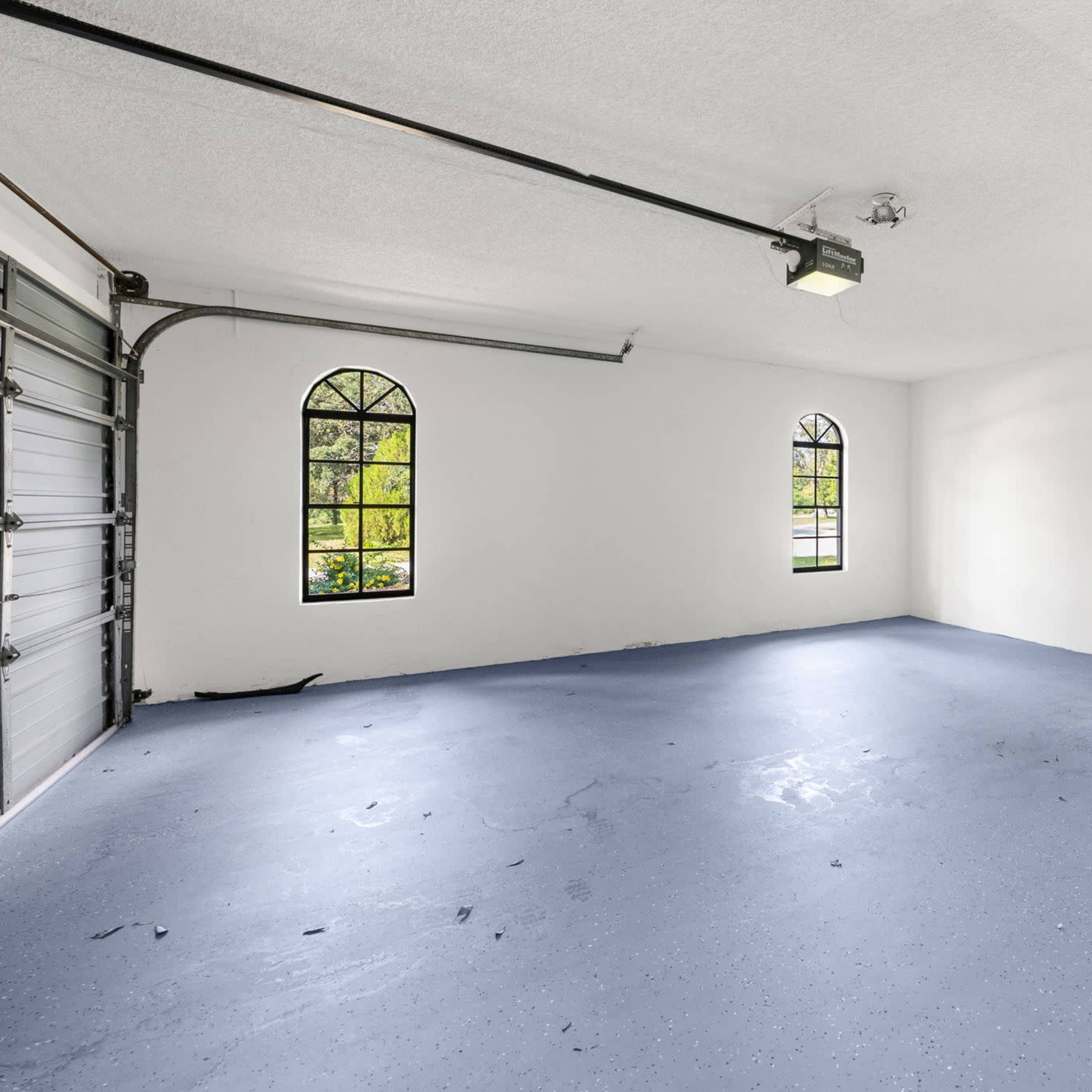 A spacious, empty garage with a blue floor and two arched windows letting in natural light.