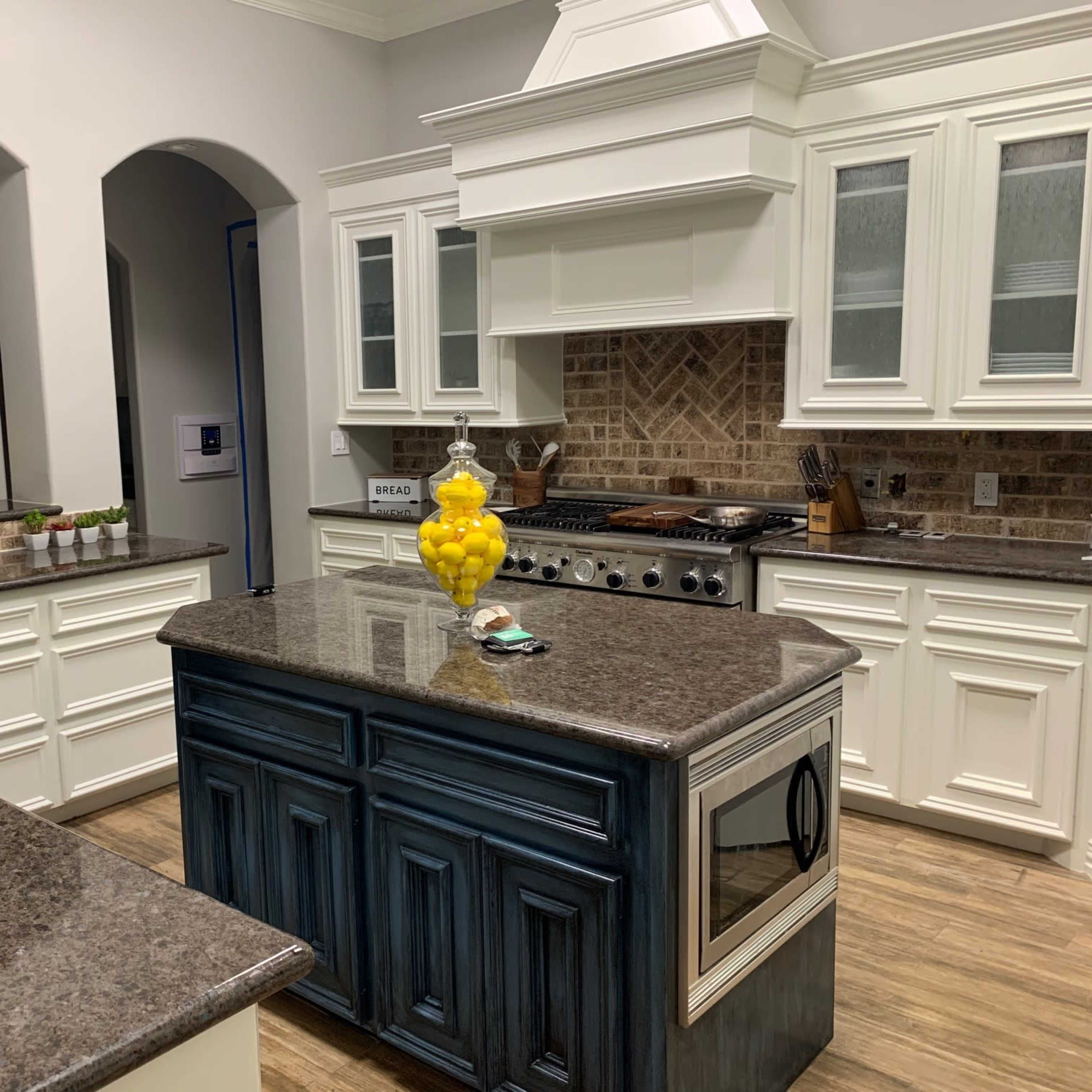 A modern kitchen with white cabinetry, a large dark countertop island, and a background of brick tiling.