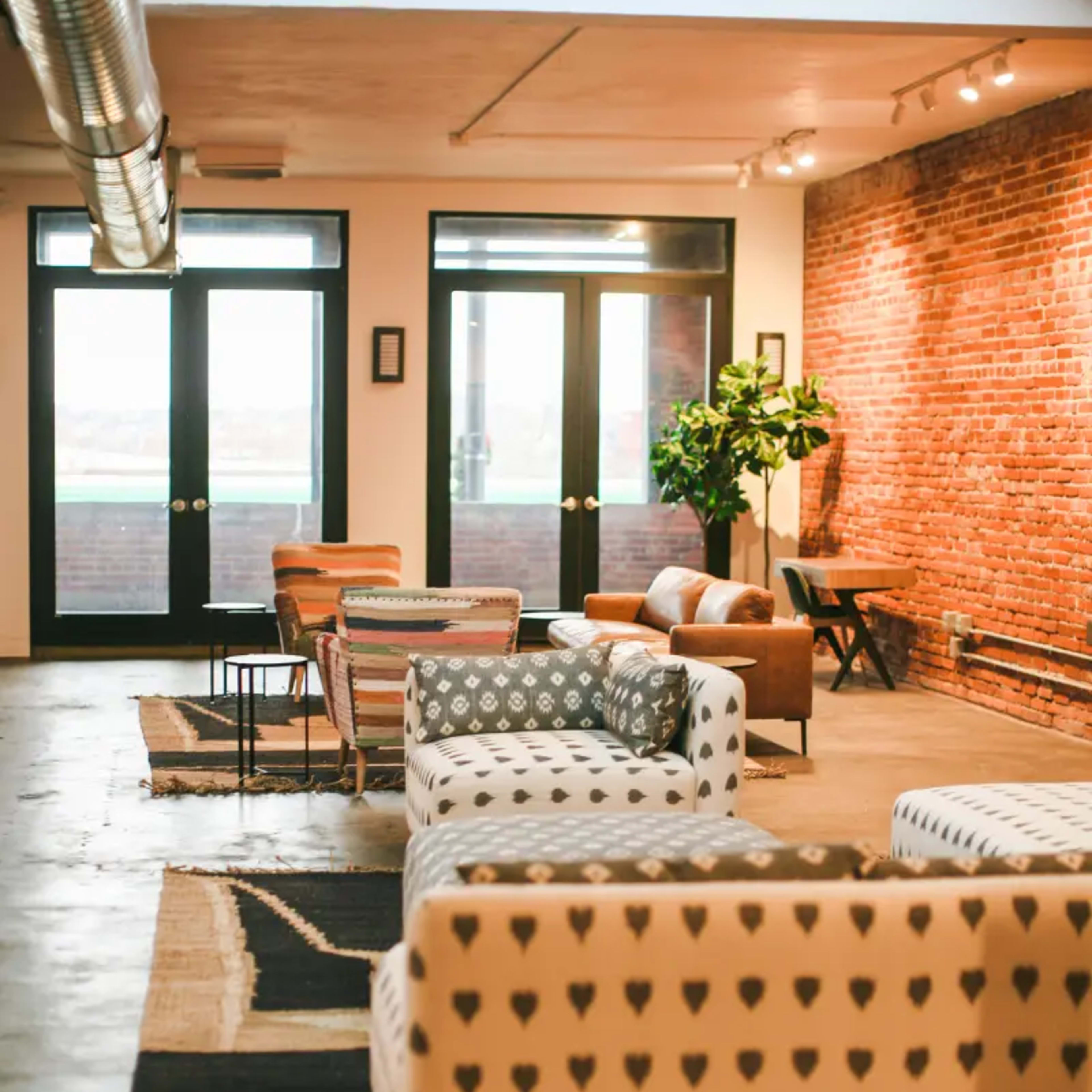 A spacious room with various patterned chairs, a small table, and large windows facing a brick wall.