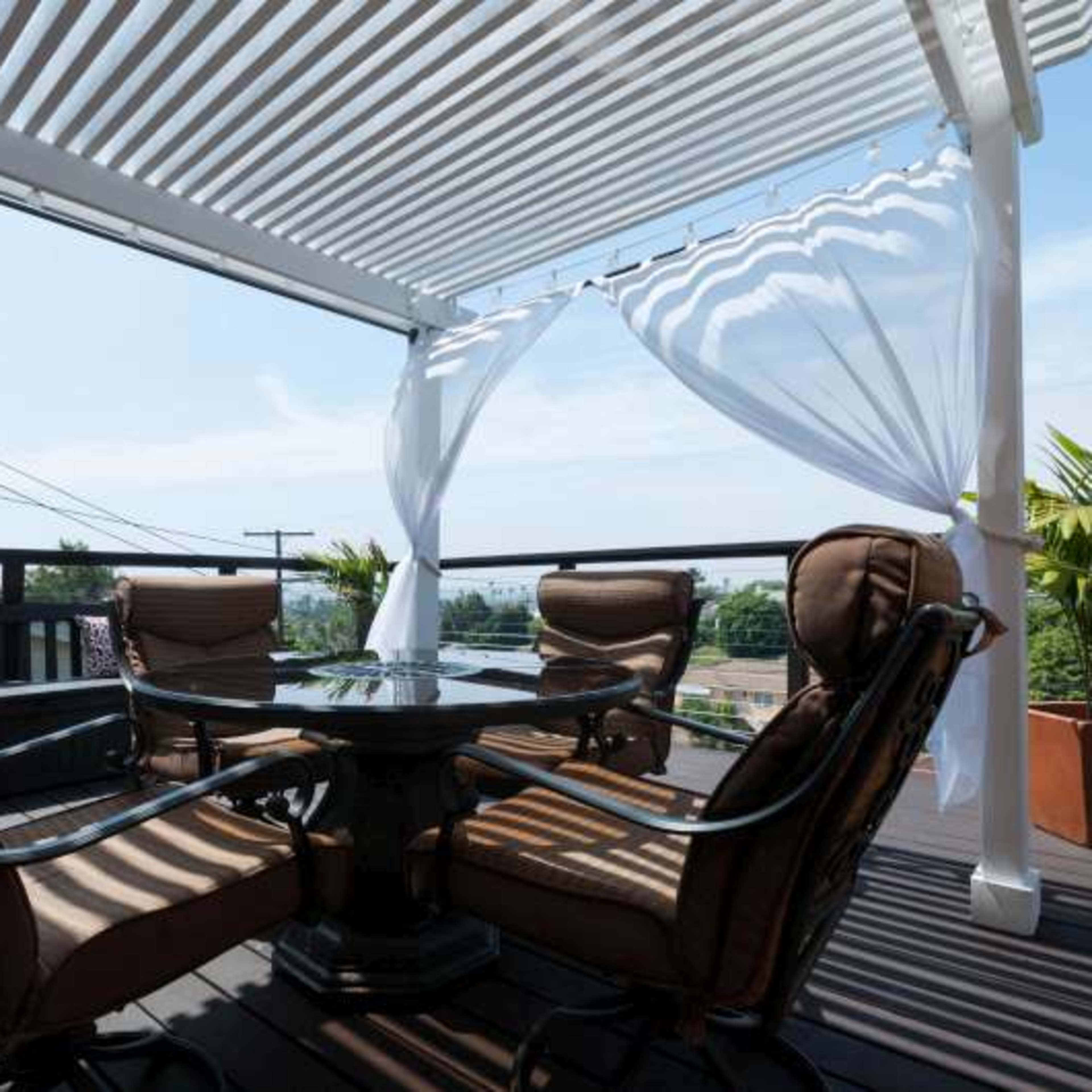A patio with a round table surrounded by four cushioned chairs, covered by a retractable canopy and overlooking a scenic view.