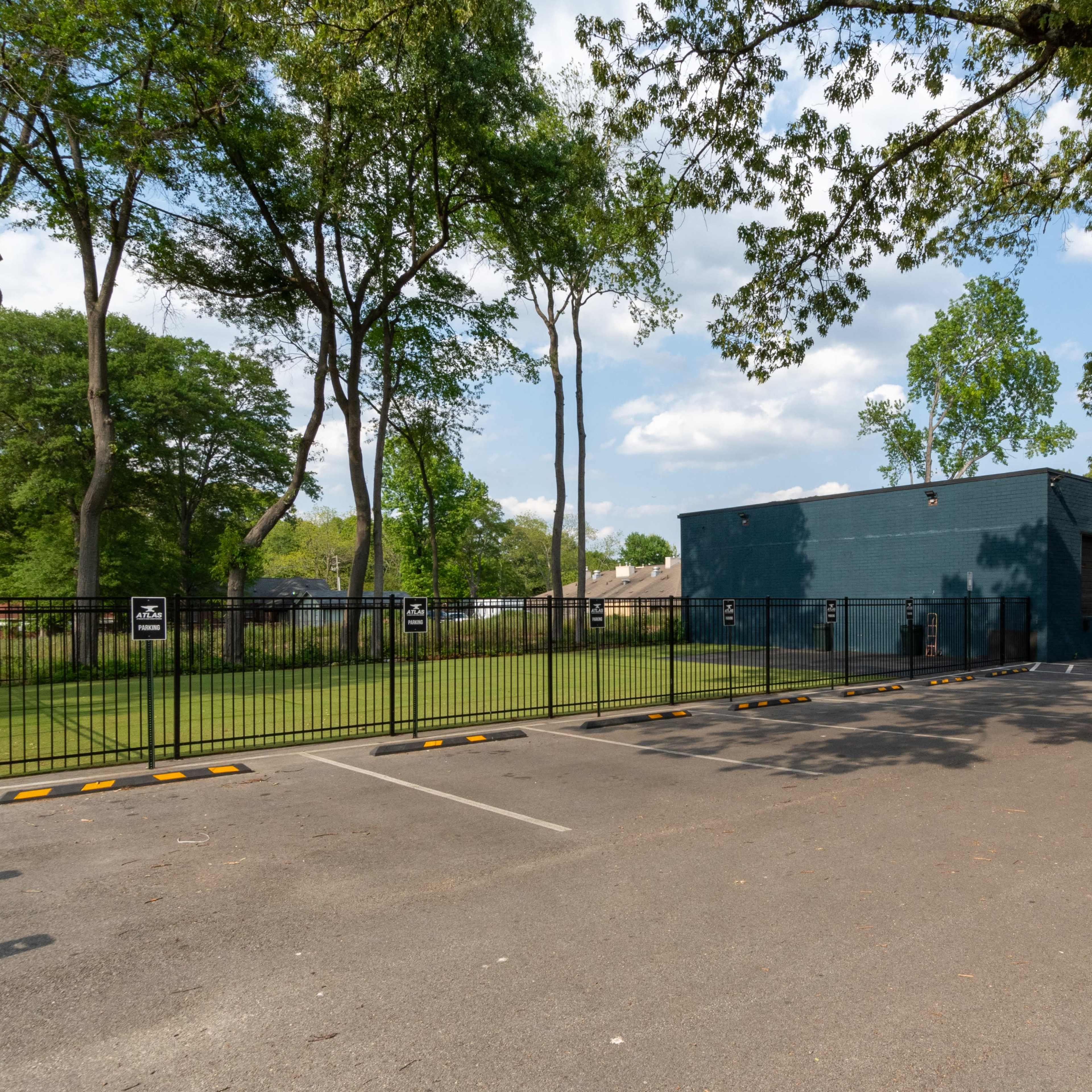 A dark blue building surrounded by trees, with a gated entrance visible from a paved parking lot.