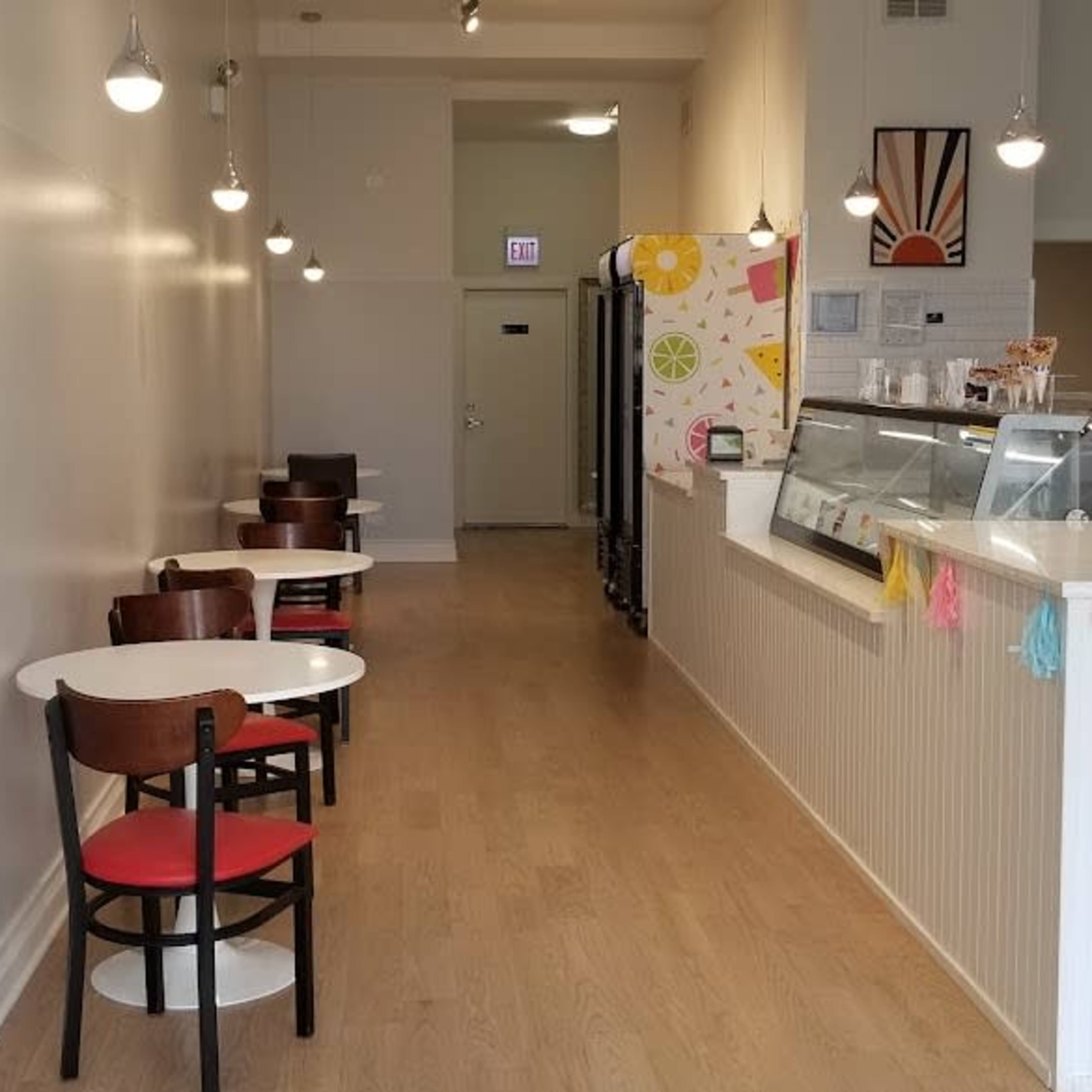 A narrow café interior with a row of tables and chairs on one side and a service counter with a display case on the other.