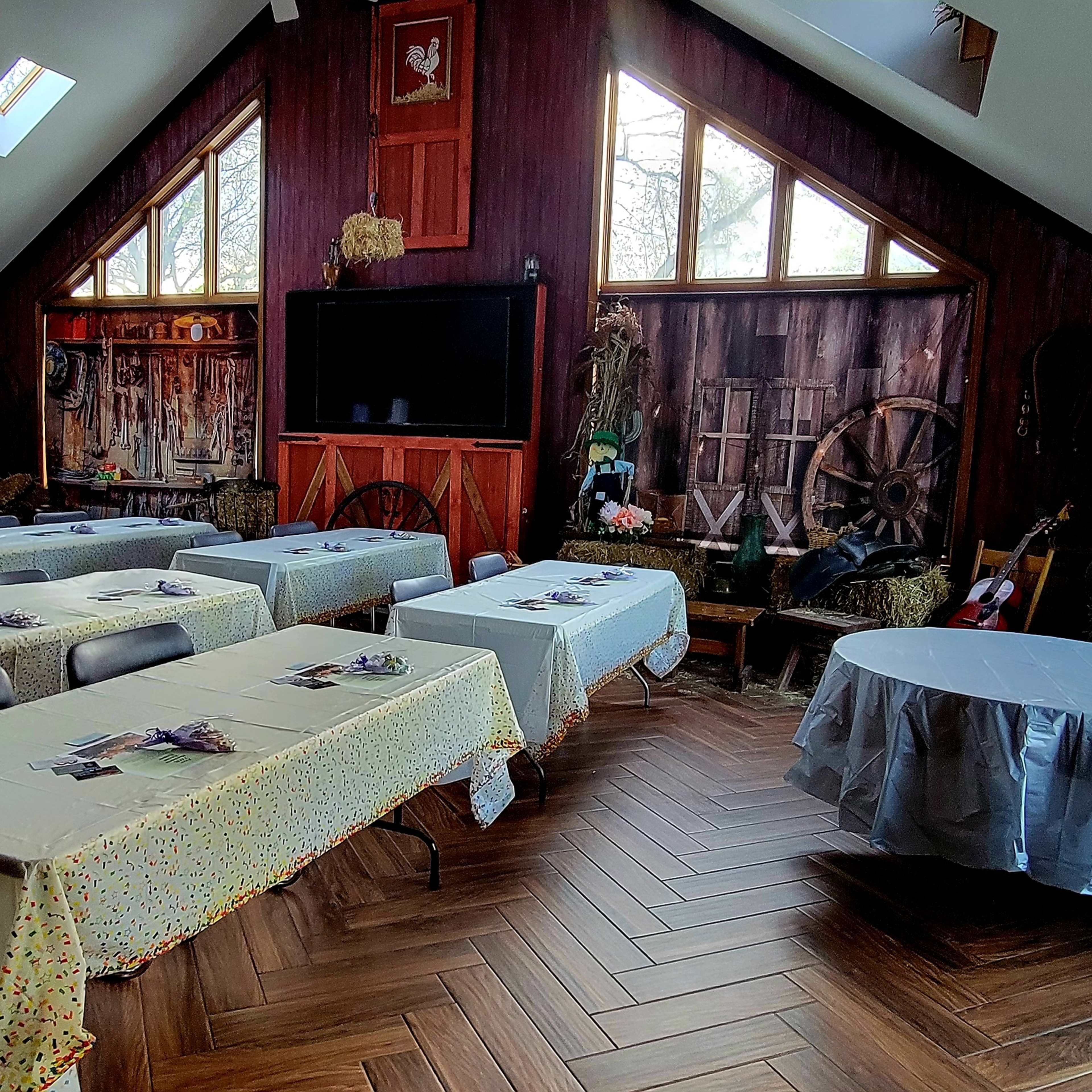 A spacious, rustic-looking room set up with several tables covered in white tablecloths, arranged for an event.