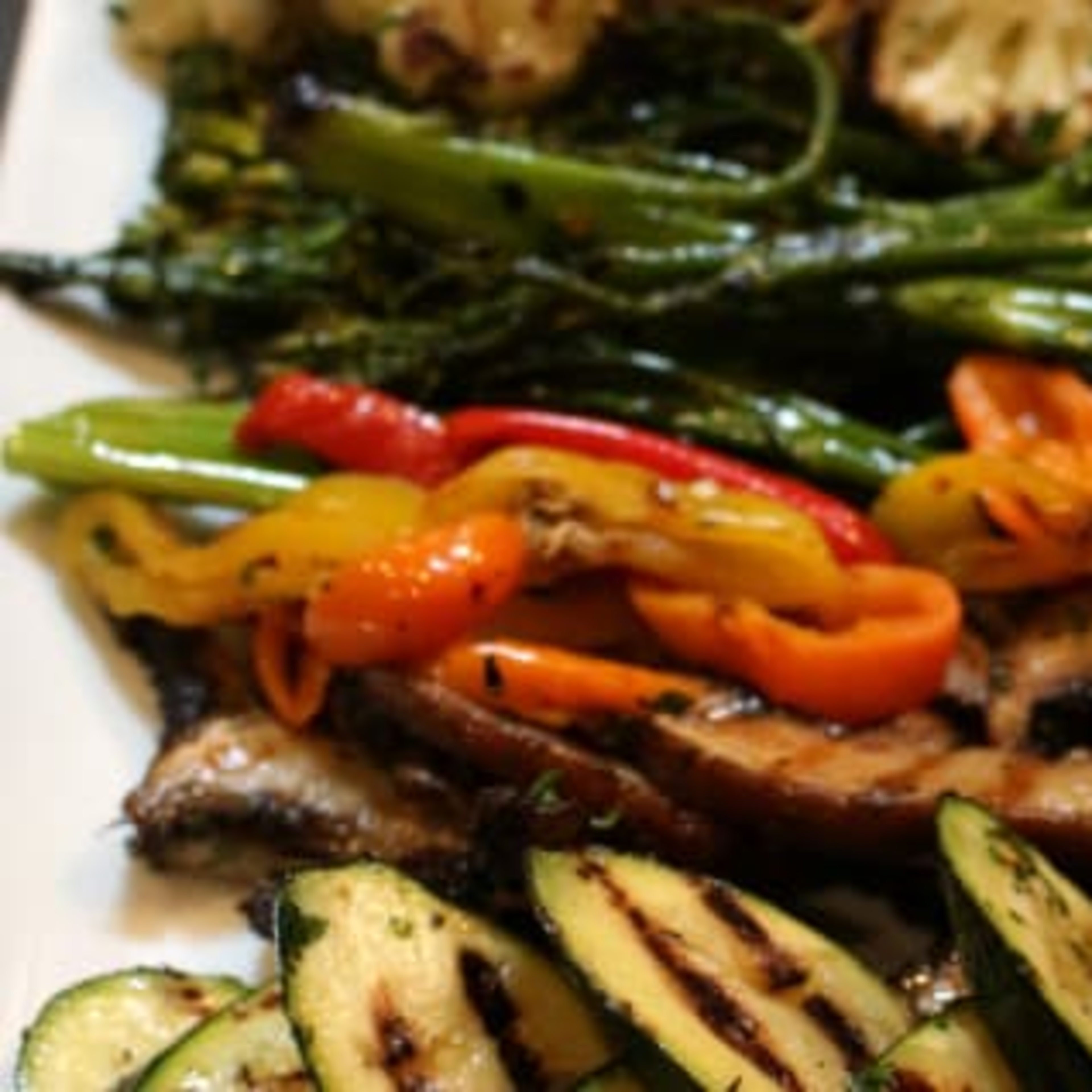 A platter of grilled vegetables, including zucchini, mini bell peppers, broccoli, and cauliflower, alongside grilled mushrooms.