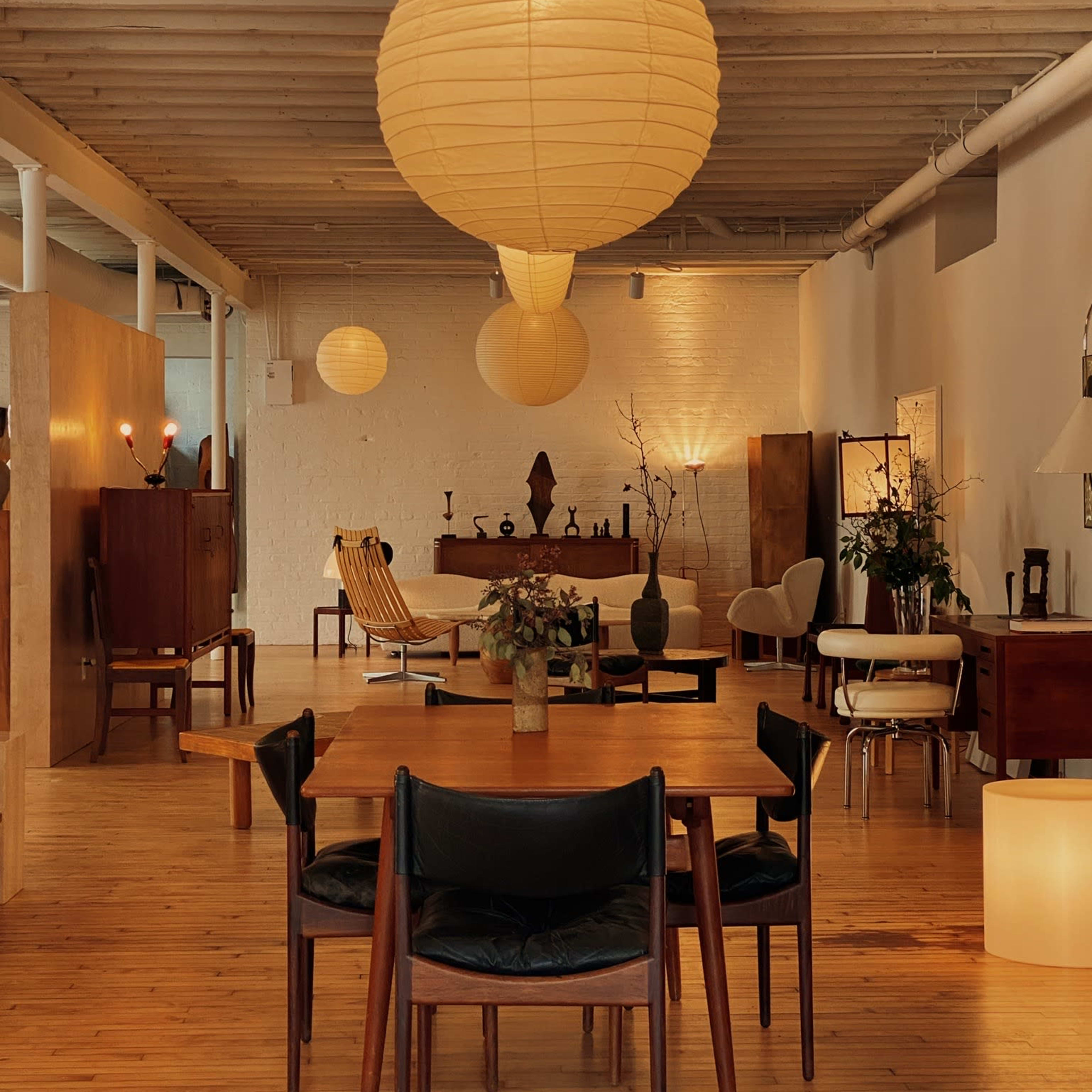 A spacious room features wooden flooring and mid-century furniture, highlighted by large paper lanterns hanging from the ceiling.
