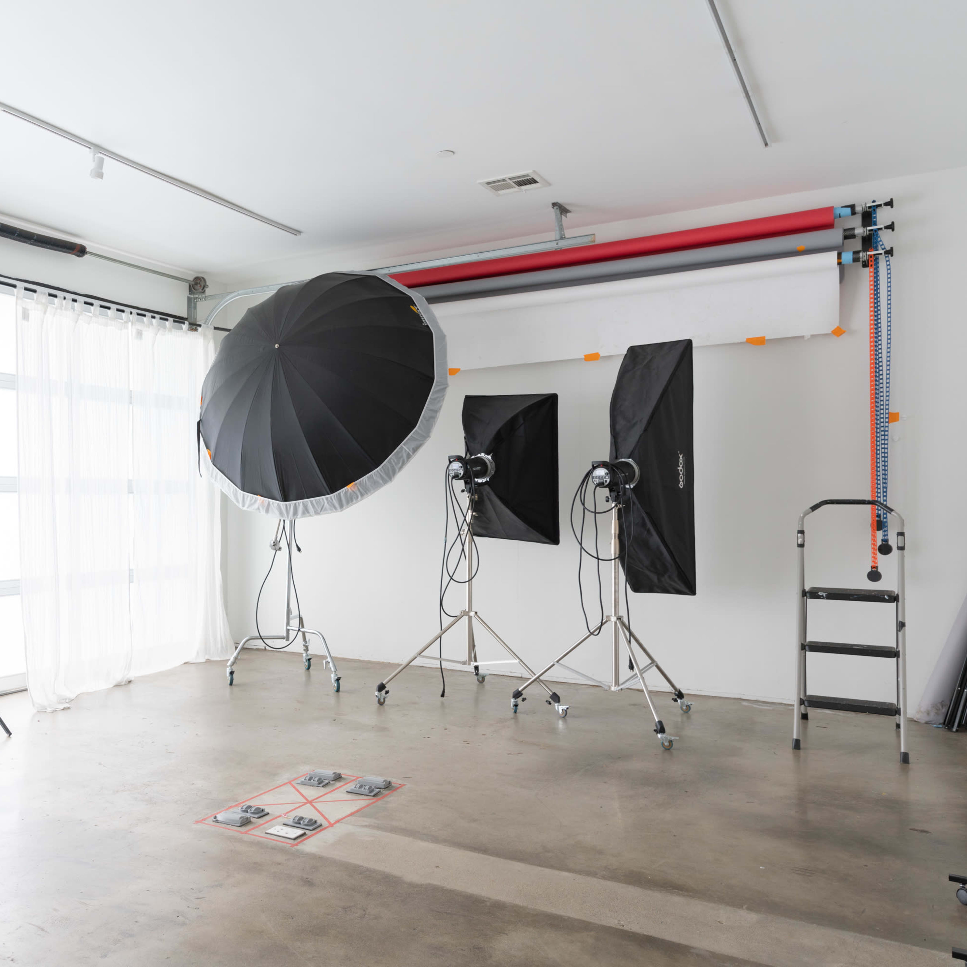 A photography studio features large softbox lights, a backdrop system, and a simple cart in a spacious, well-lit room.