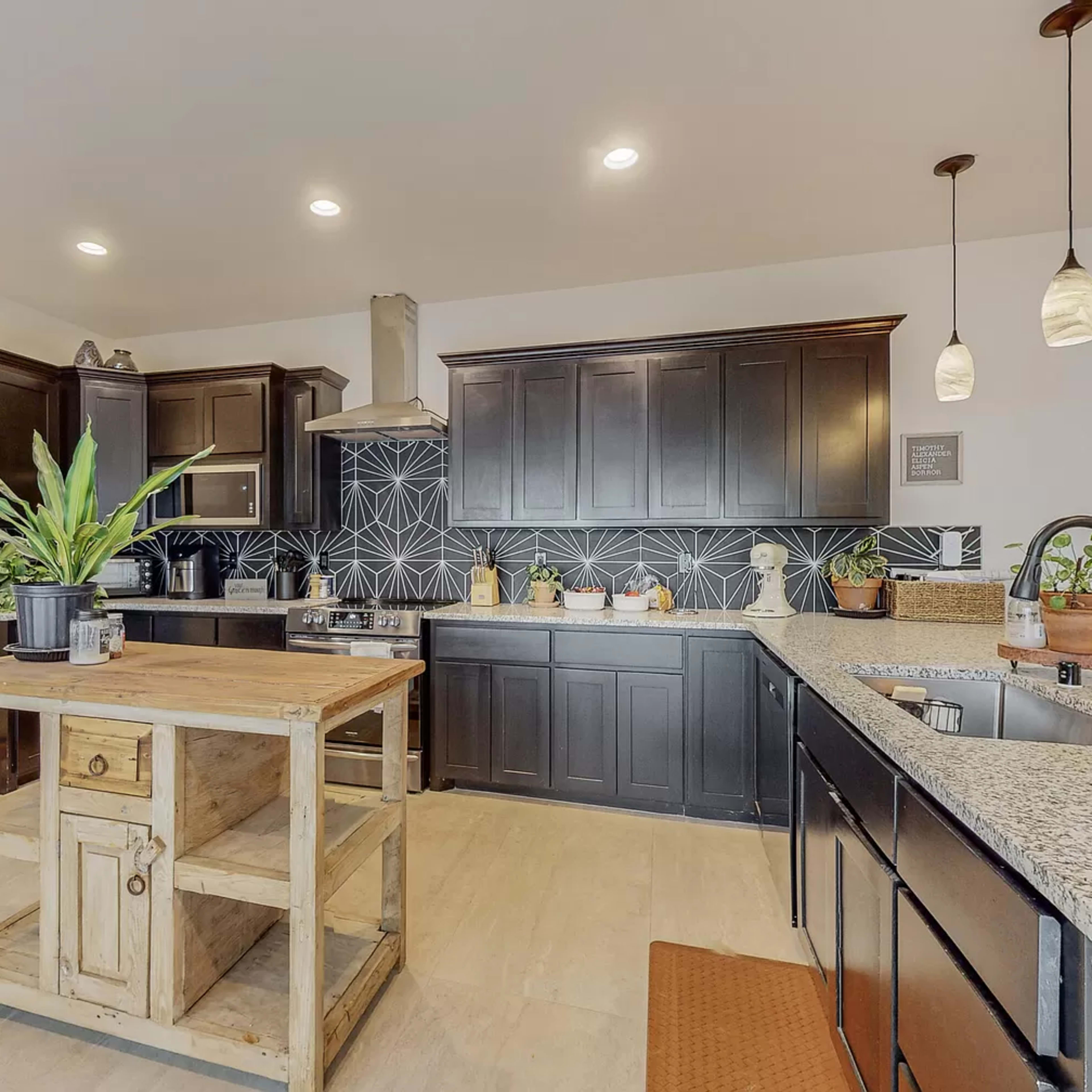 The kitchen features dark cabinetry, a central wooden island, and a geometric backsplash.
