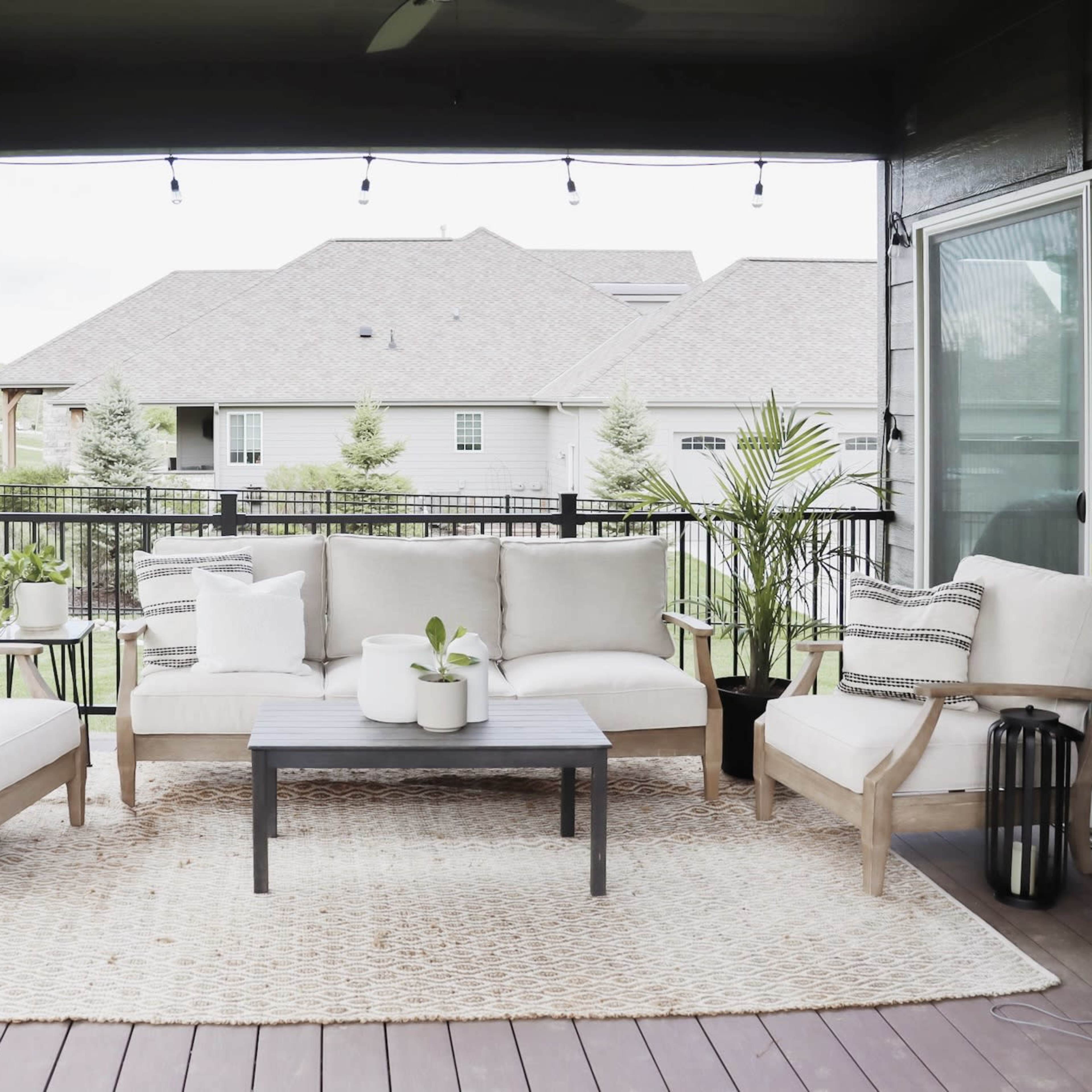 A spacious outdoor seating area features beige furniture, a coffee table, potted plants, and a jute rug on a wooden deck.