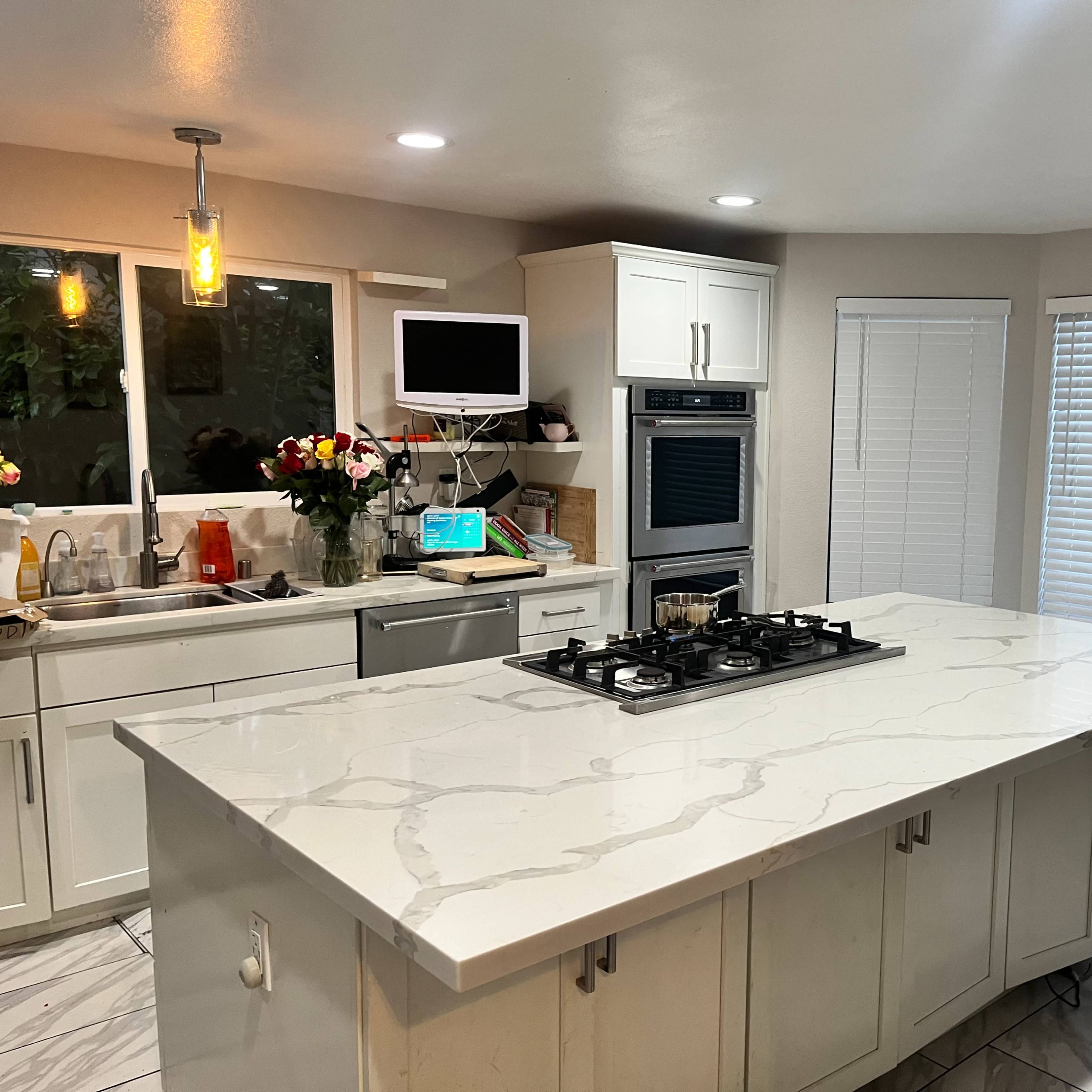 A modern kitchen with a central island featuring a gas cooktop, white cabinetry, and a window above the sink.