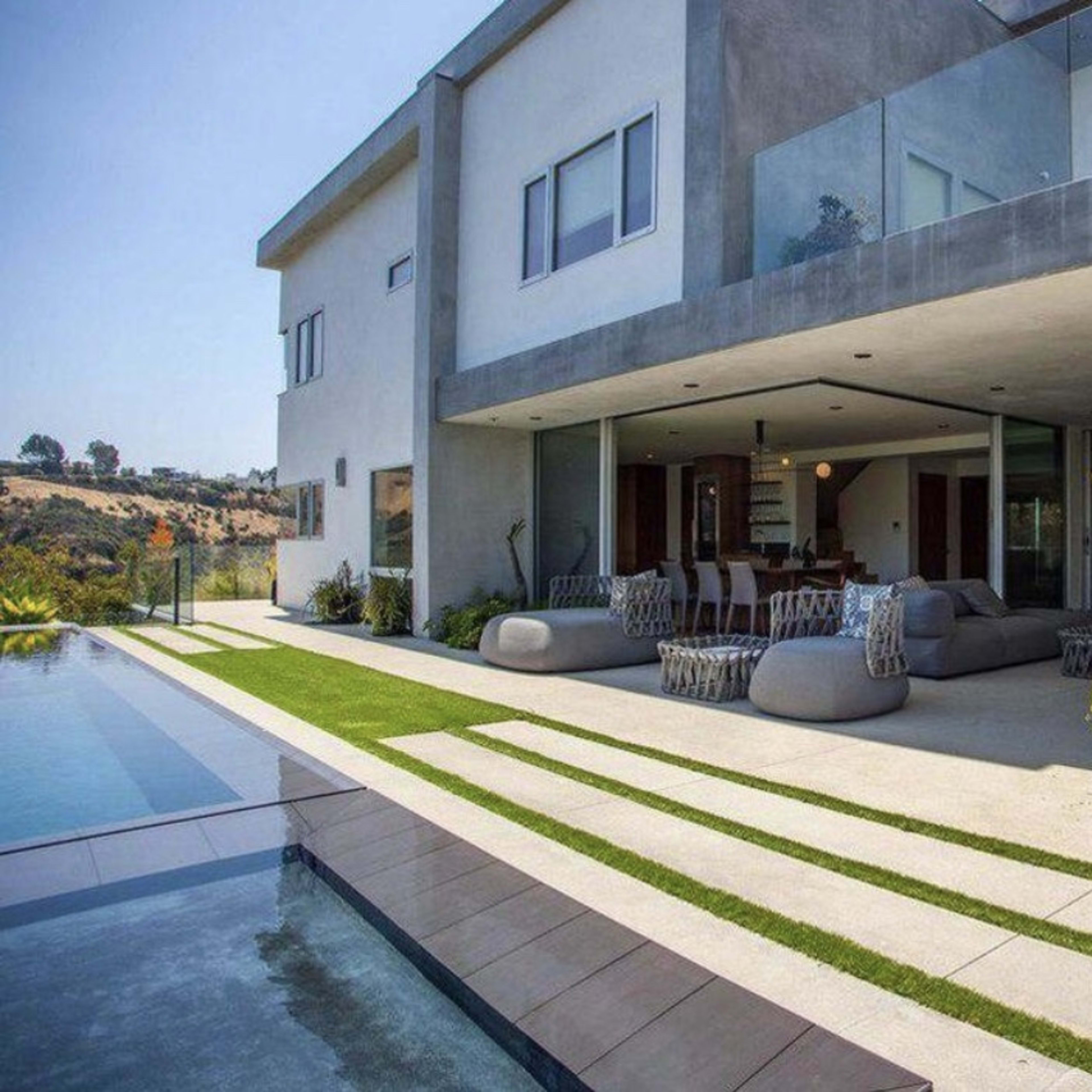 A modern house with a spacious patio, outdoor seating, and a swimming pool surrounded by landscaped greenery.