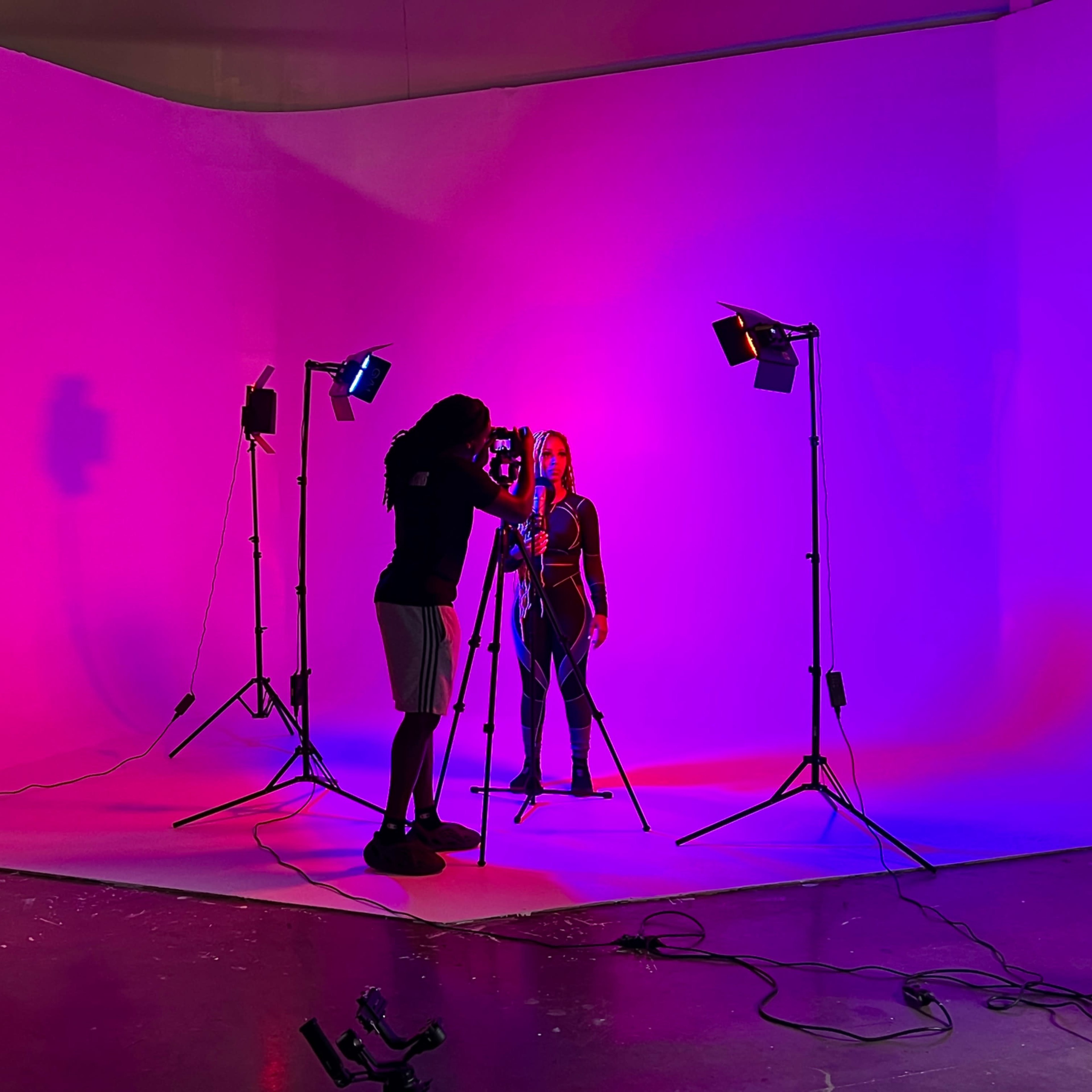 A photographer captures an image of a model in a brightly lit studio with pink and blue backgrounds.