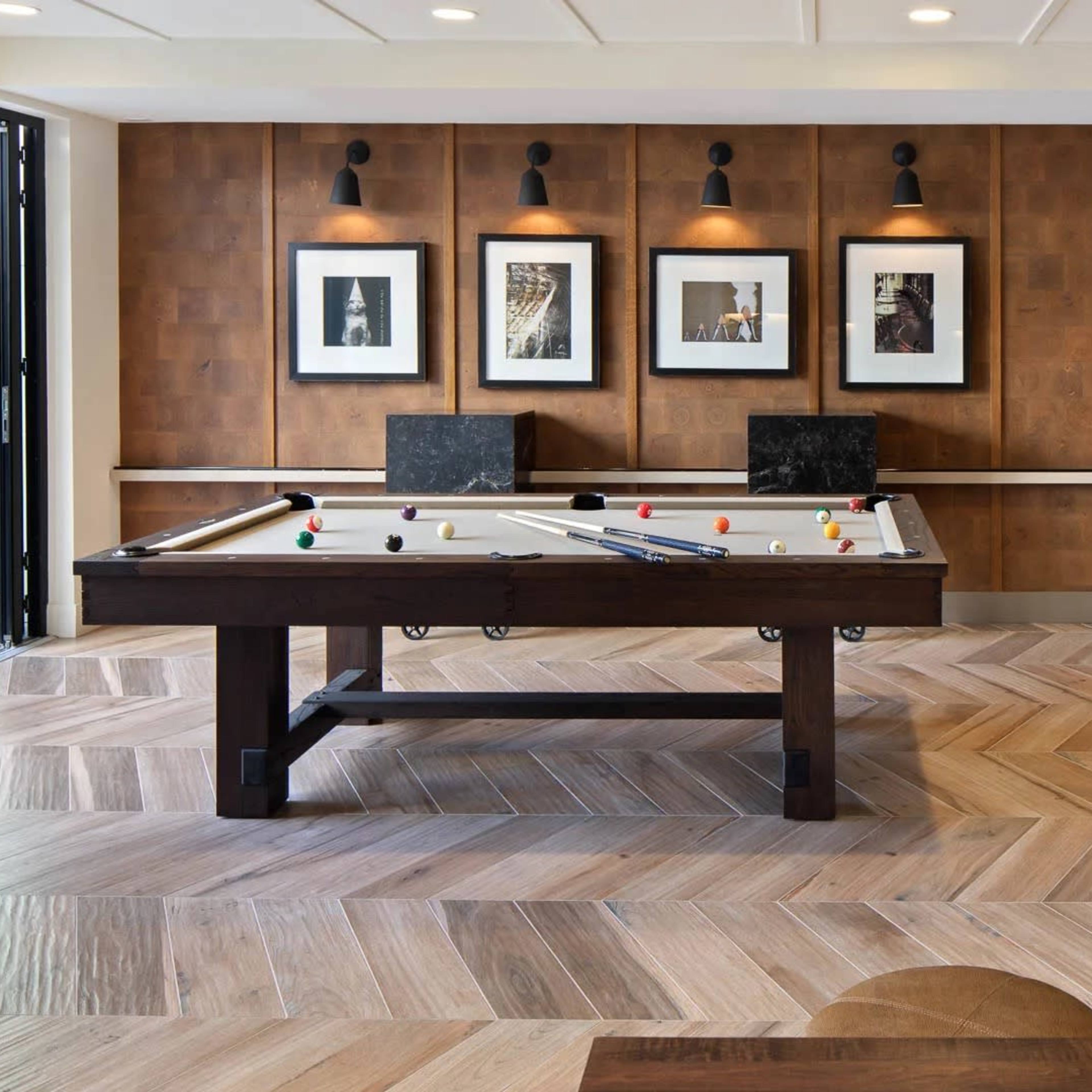 A modern game room featuring a pool table, framed artwork on the walls, a television showing a sports game, and a cozy seating area with decorative elements.