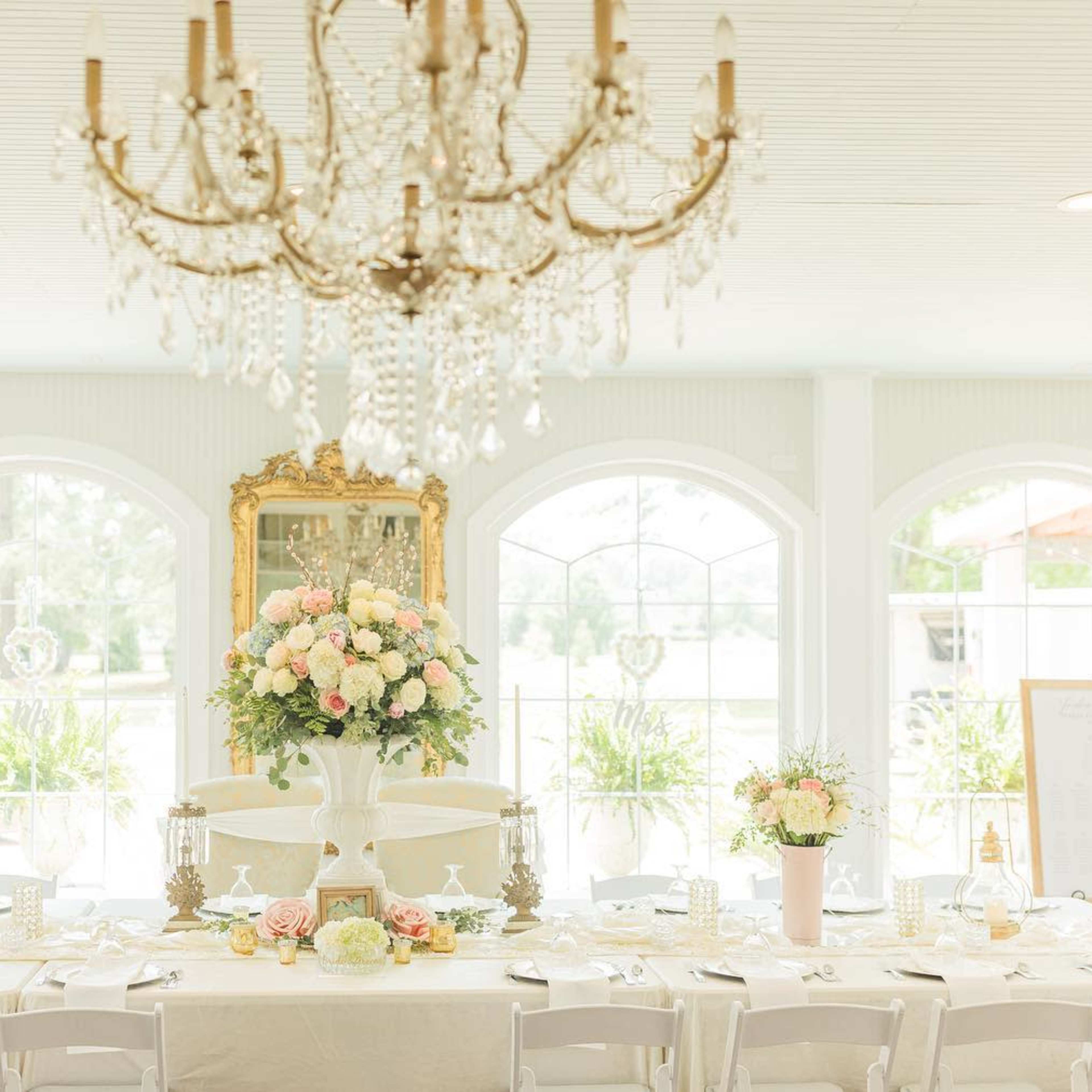 A spacious dining area features a long table set with decorative floral arrangements, elegant tableware, and a large chandelier overhead.