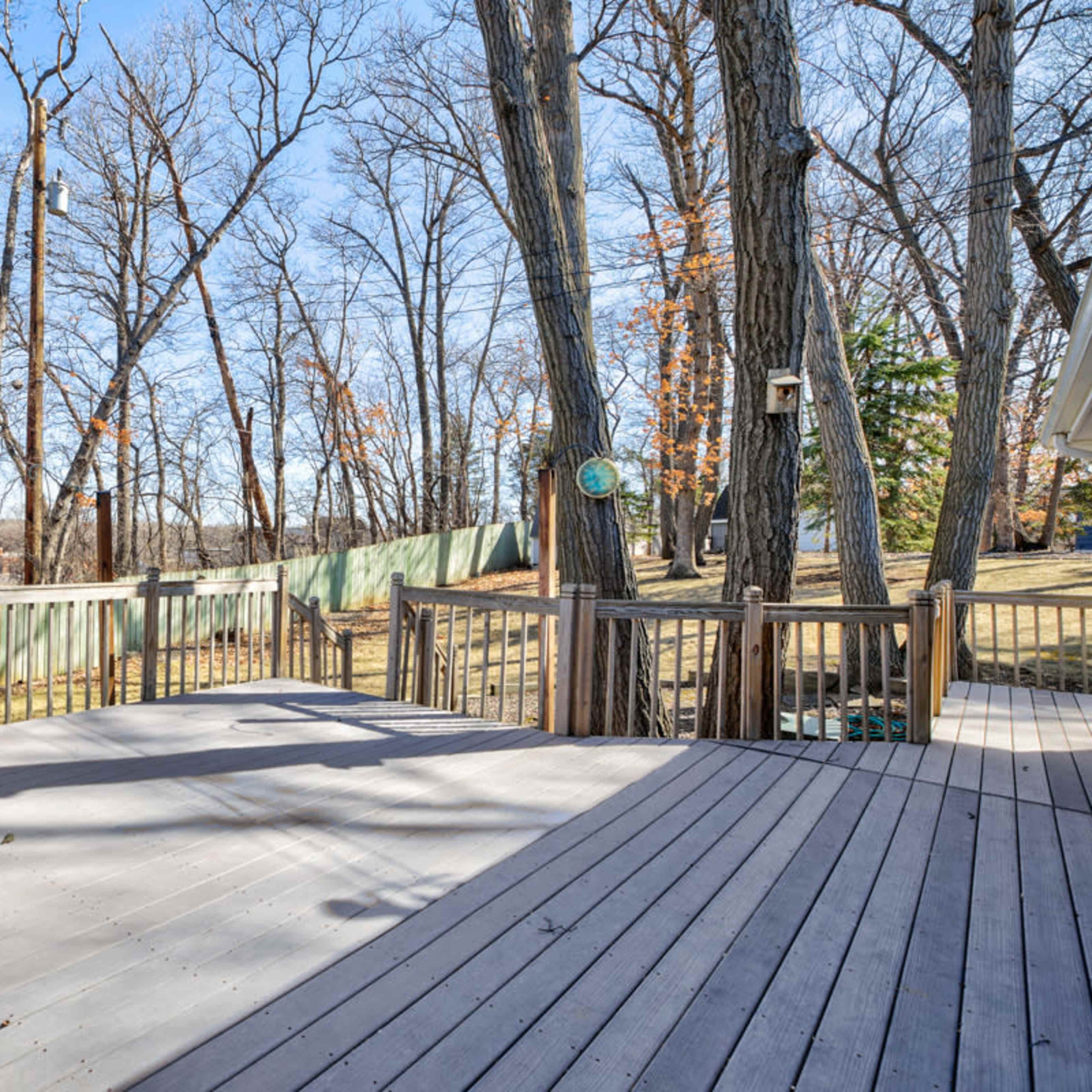 A wooden deck is surrounded by bare trees and a green fence in a clear outdoor setting.