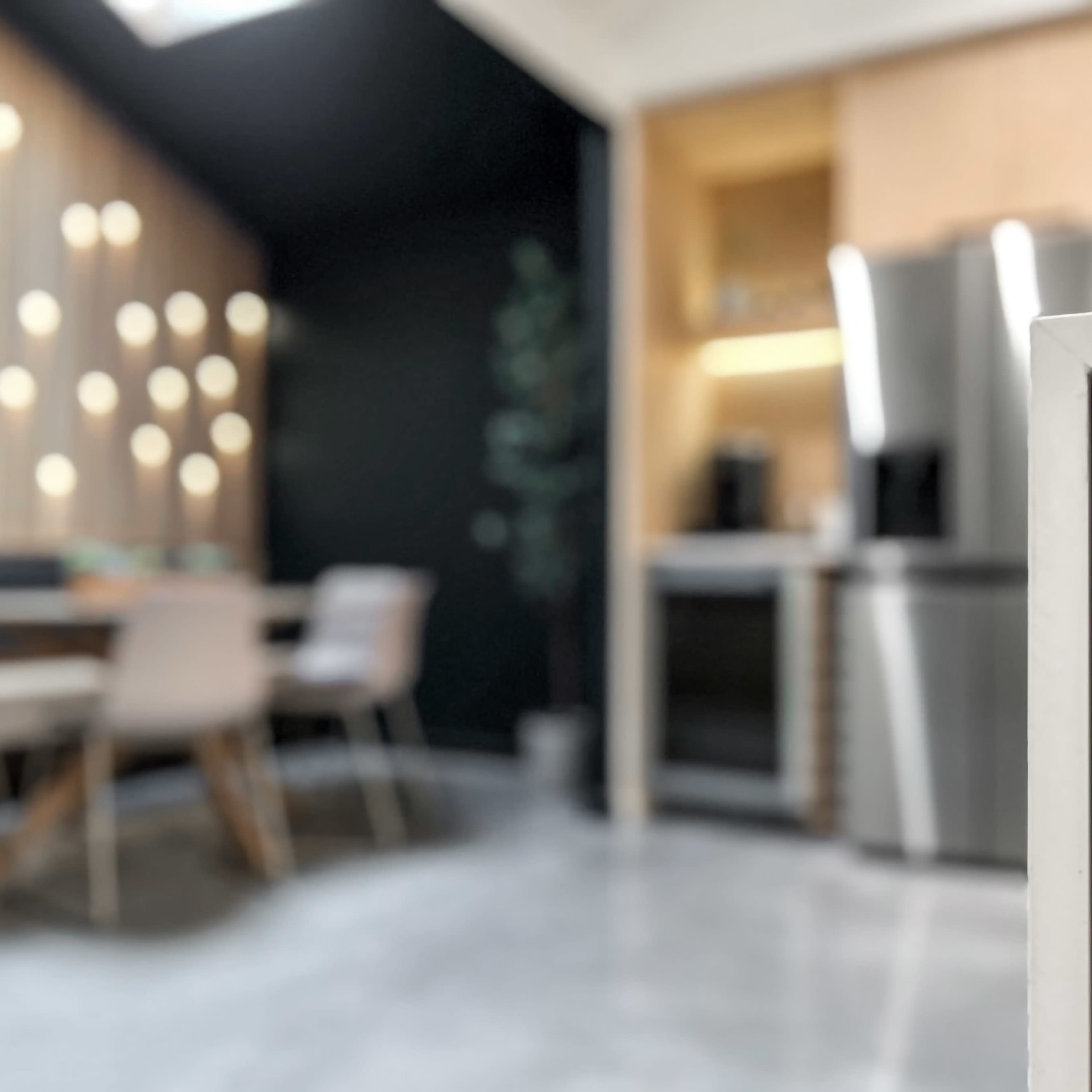 A blurred modern kitchen with a wooden dining table and chairs in the foreground, featuring stainless steel appliances in the background.