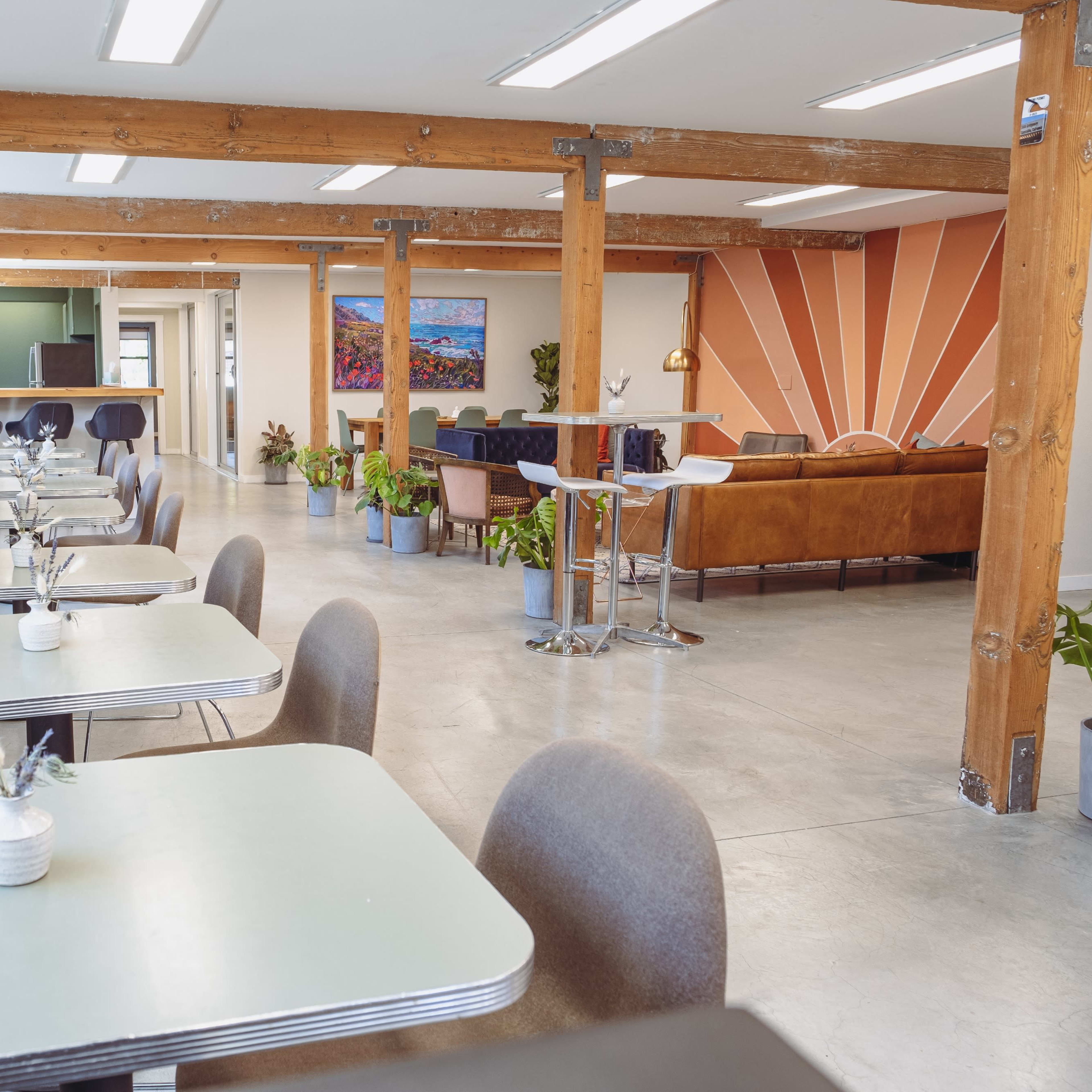 A modern café interior with neatly arranged tables, minimalist decor, wooden beams, and potted plants.