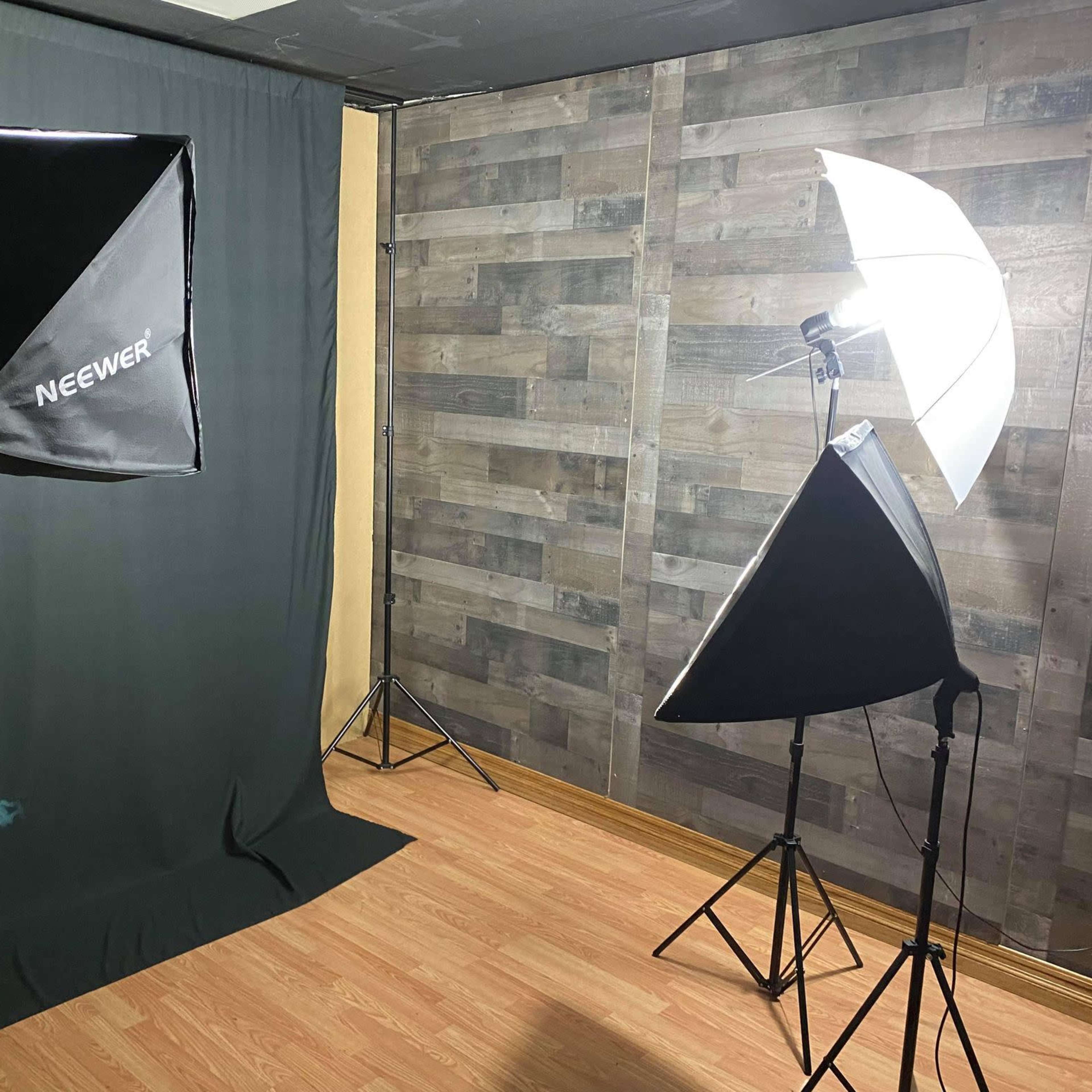 A photography studio setup with two lighting umbrellas and a green backdrop against a wooden wall.