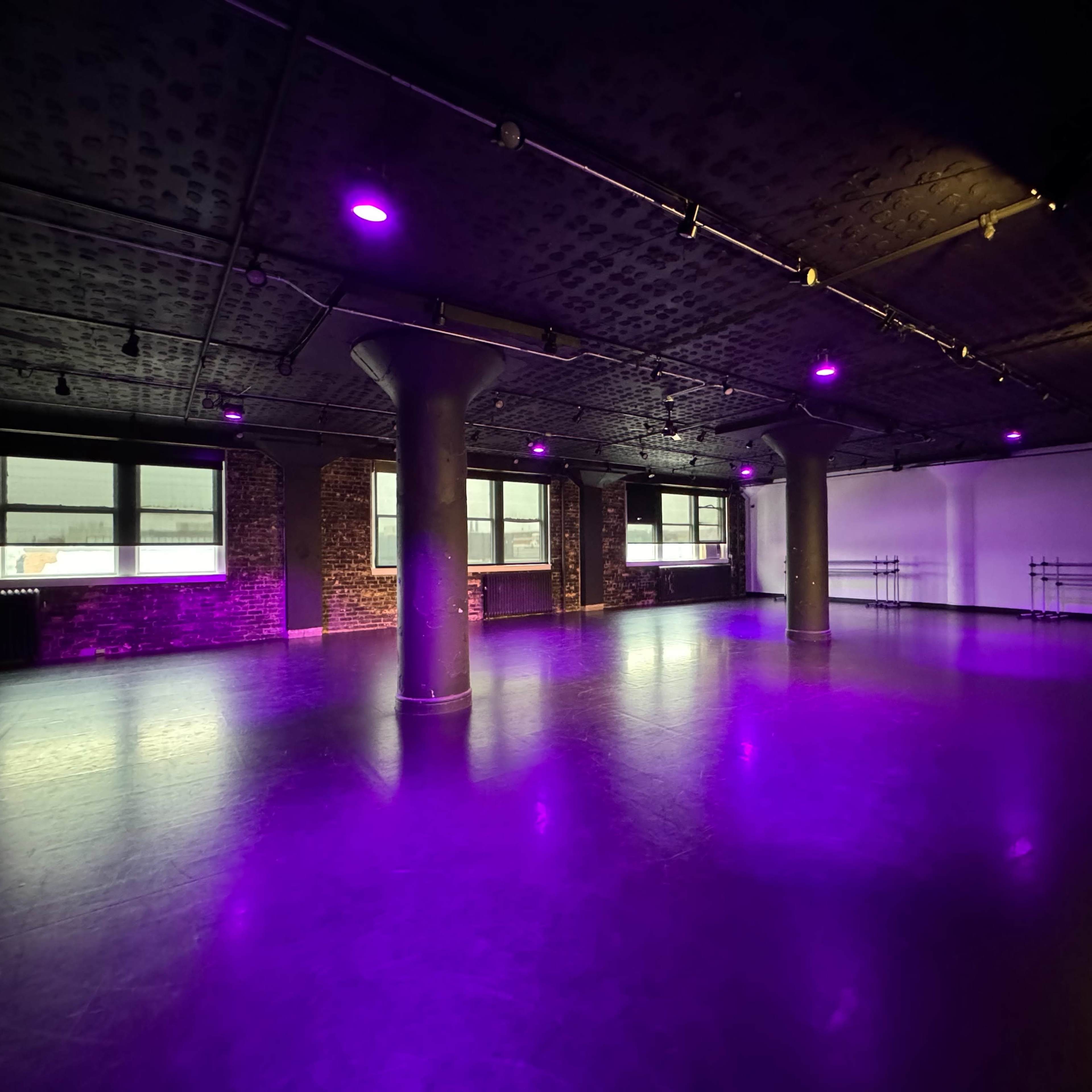 An empty studio space with purple lighting, exposed brick walls, and pillars in a large room.