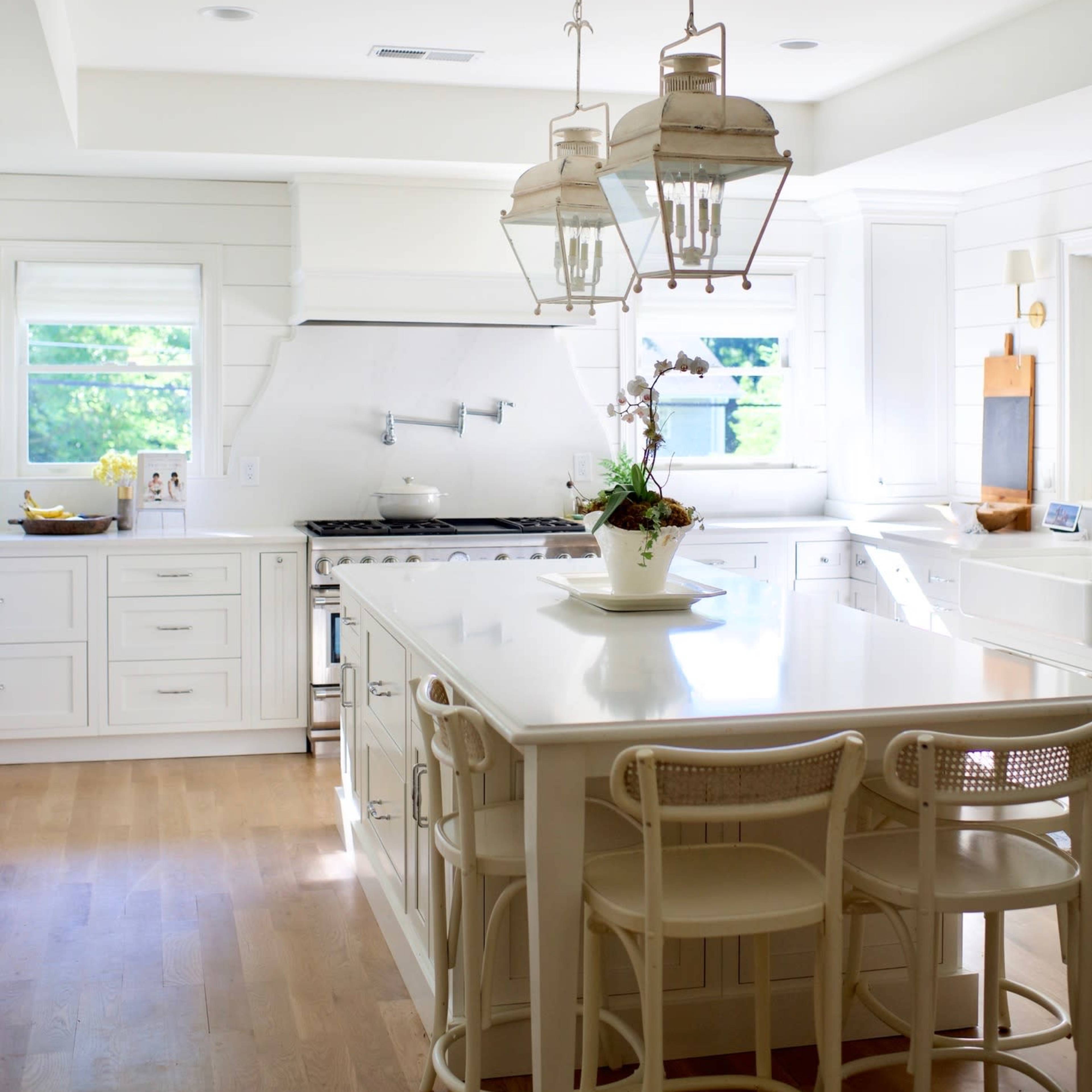 A modern kitchen features white cabinetry, a large island with bar stools, and pendant lighting above.