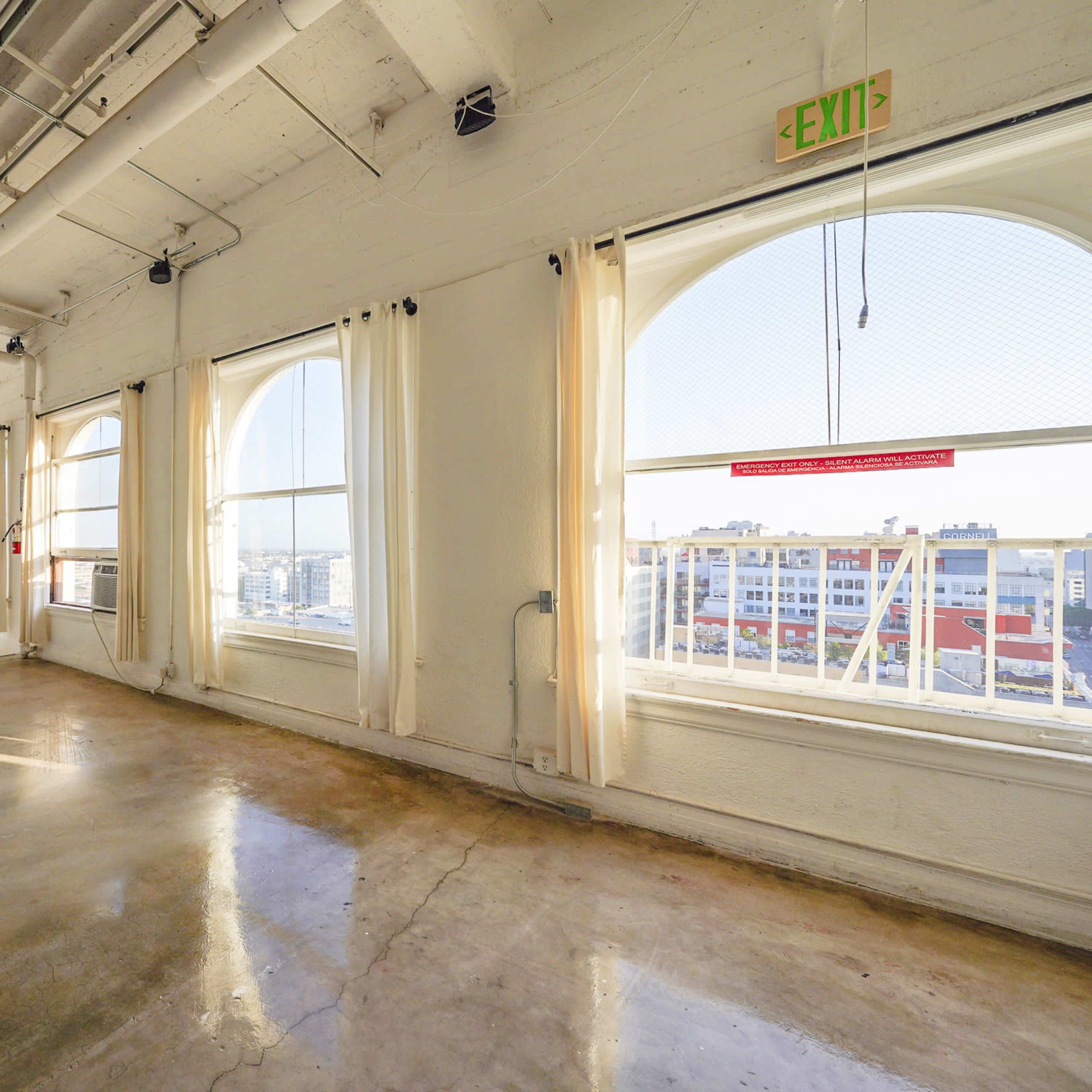 A spacious, brightly lit room with large windows, white walls, and a concrete floor.
