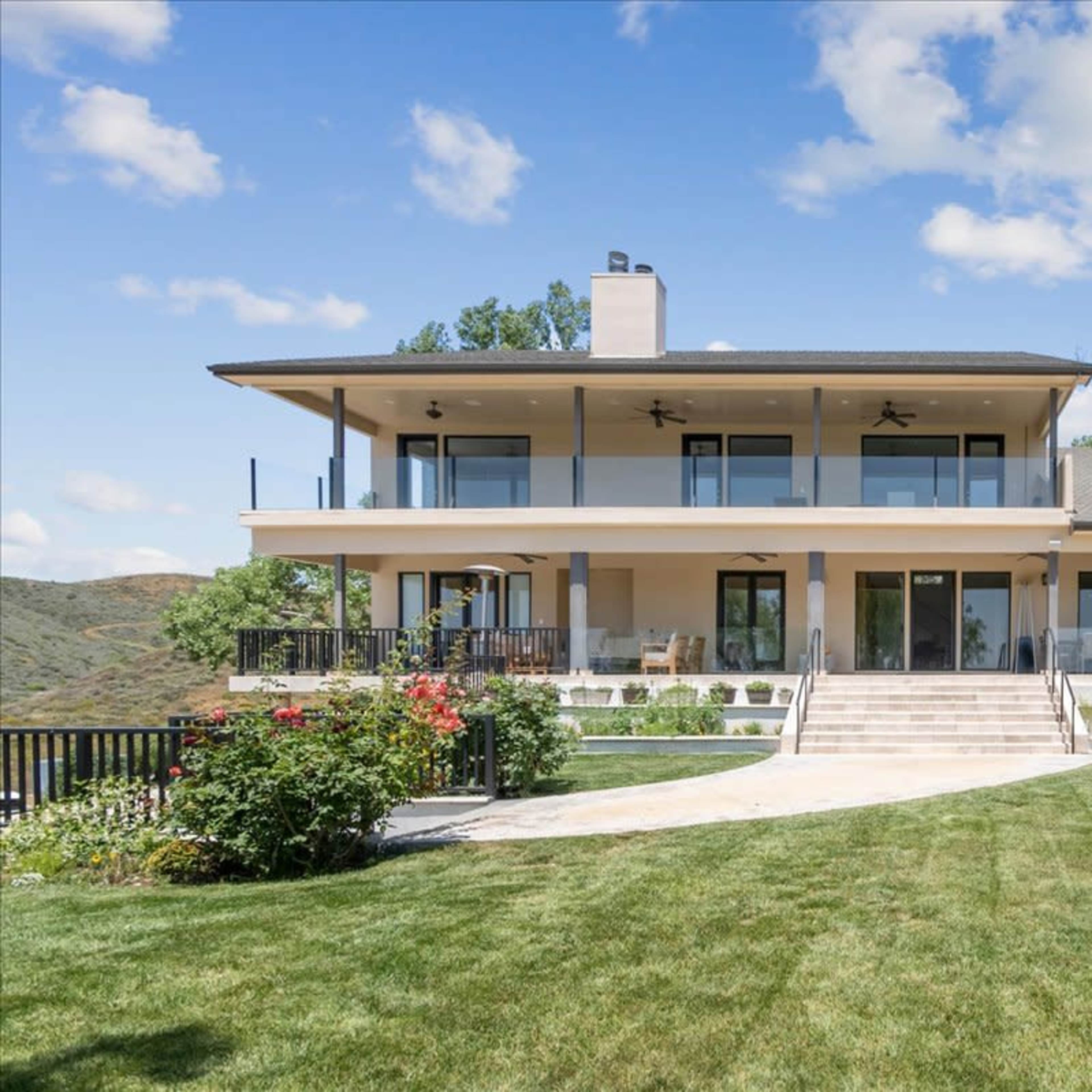 A modern two-story house with a spacious patio and landscaped yard overlooks rolling hills.