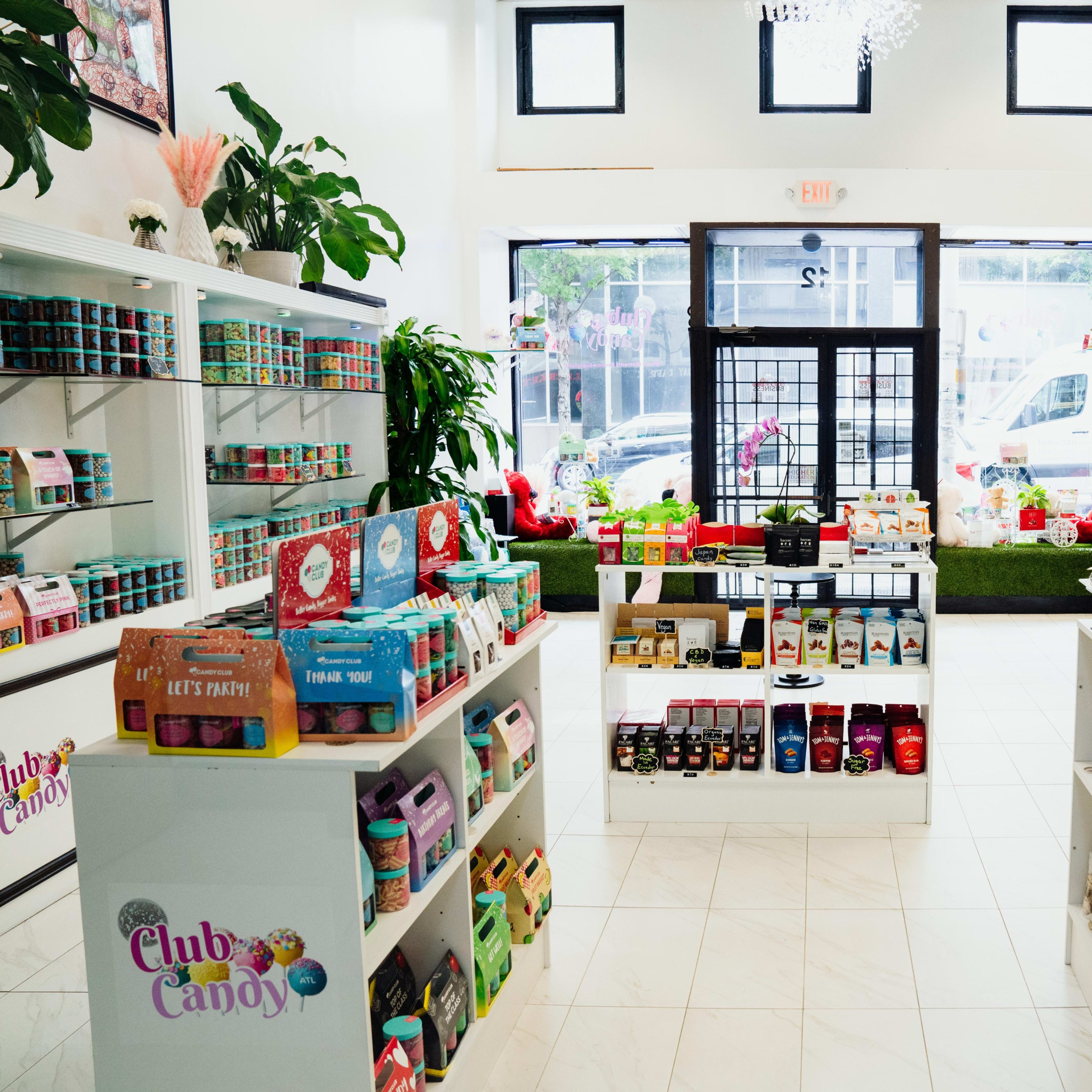 An interior of a colorful candy store with neatly arranged shelves displaying various sweets and snacks, large windows allowing natural light in, and plants enhancing the decor.
