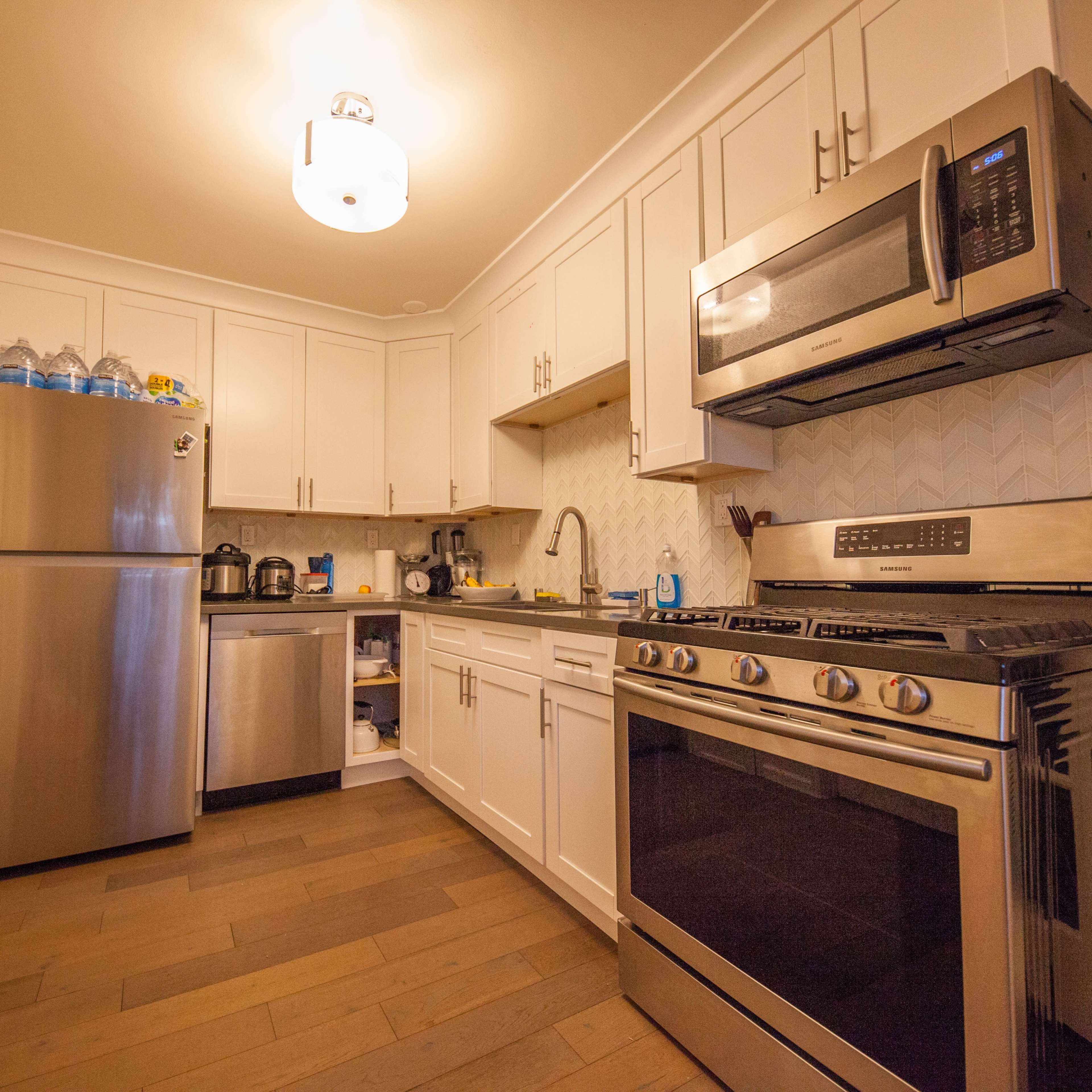 A modern kitchen with stainless steel appliances, white cabinetry, and wooden floors.