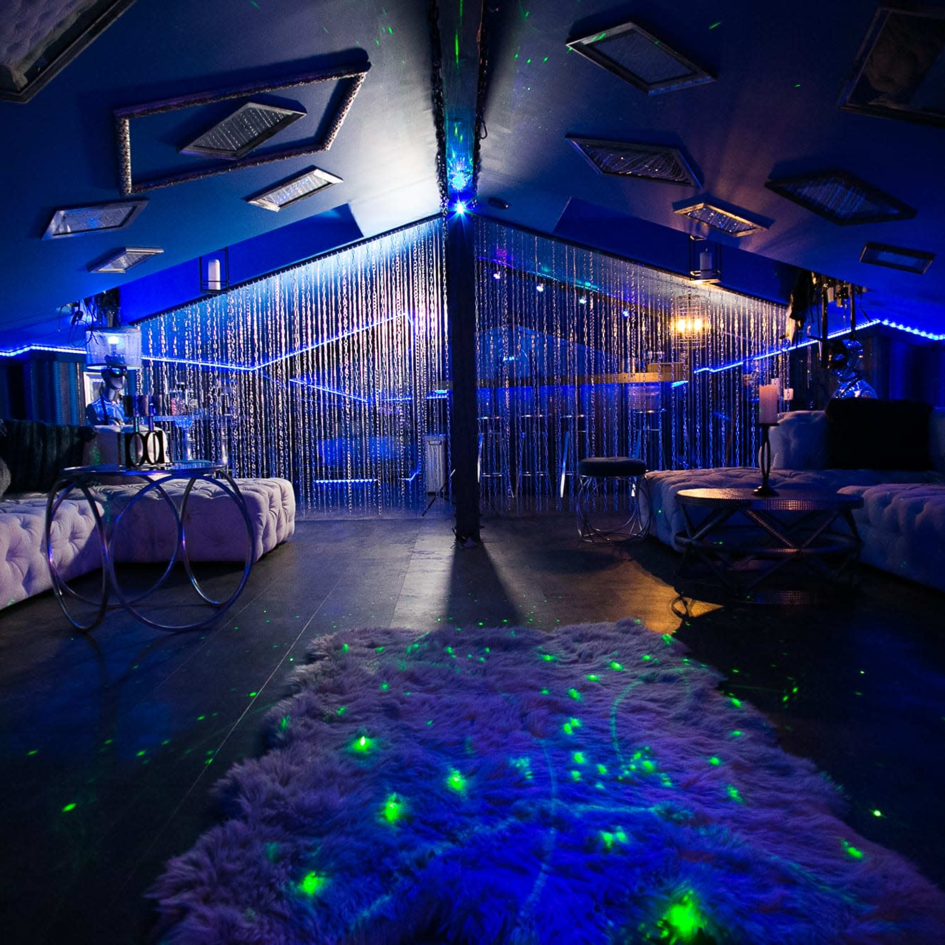 A dimly lit lounge area featuring plush seating, decorative lighting, and a curtain of beads separating different sections.