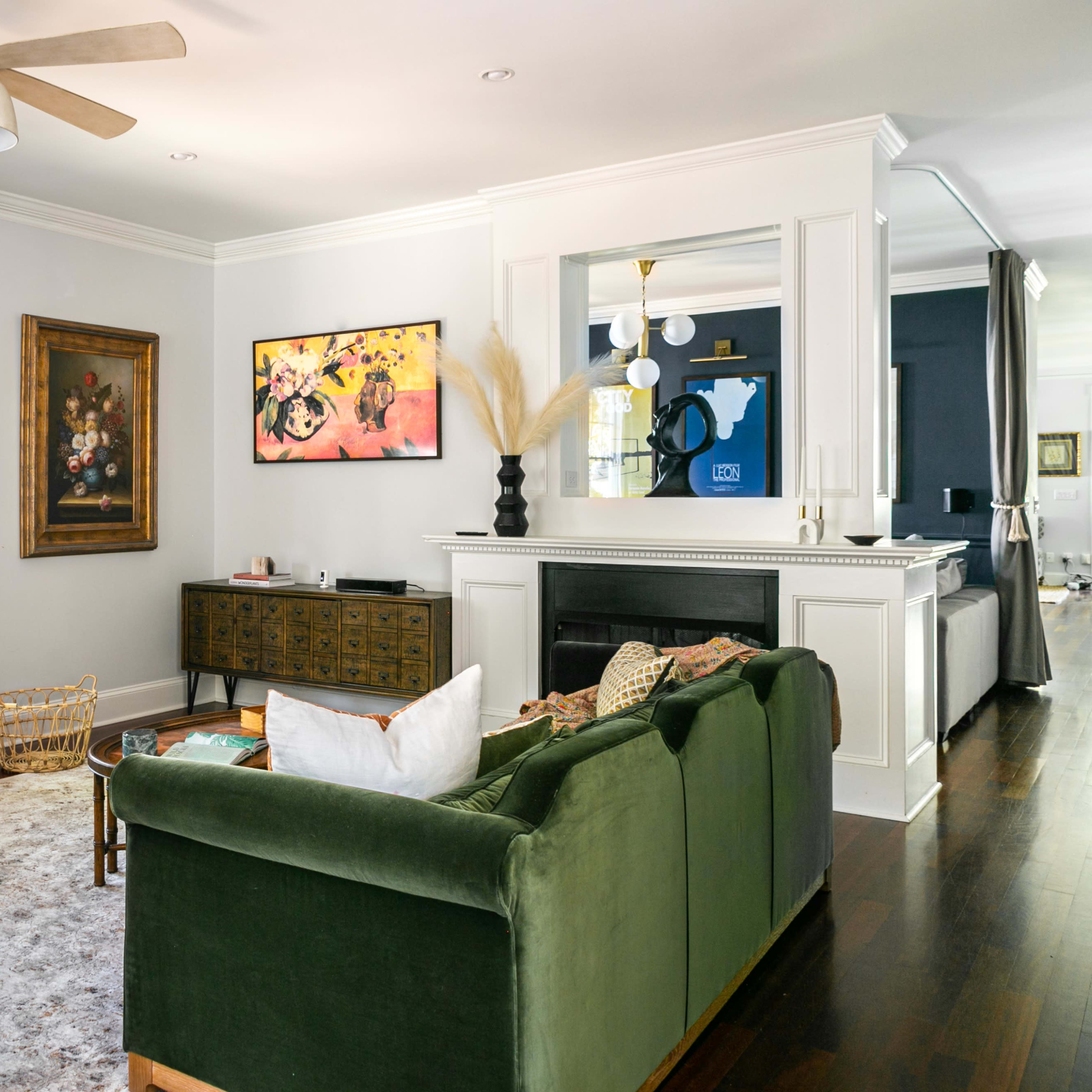 The living room features a green sofa, two wooden chairs, a coffee table, and a wall-mounted television above a fireplace.