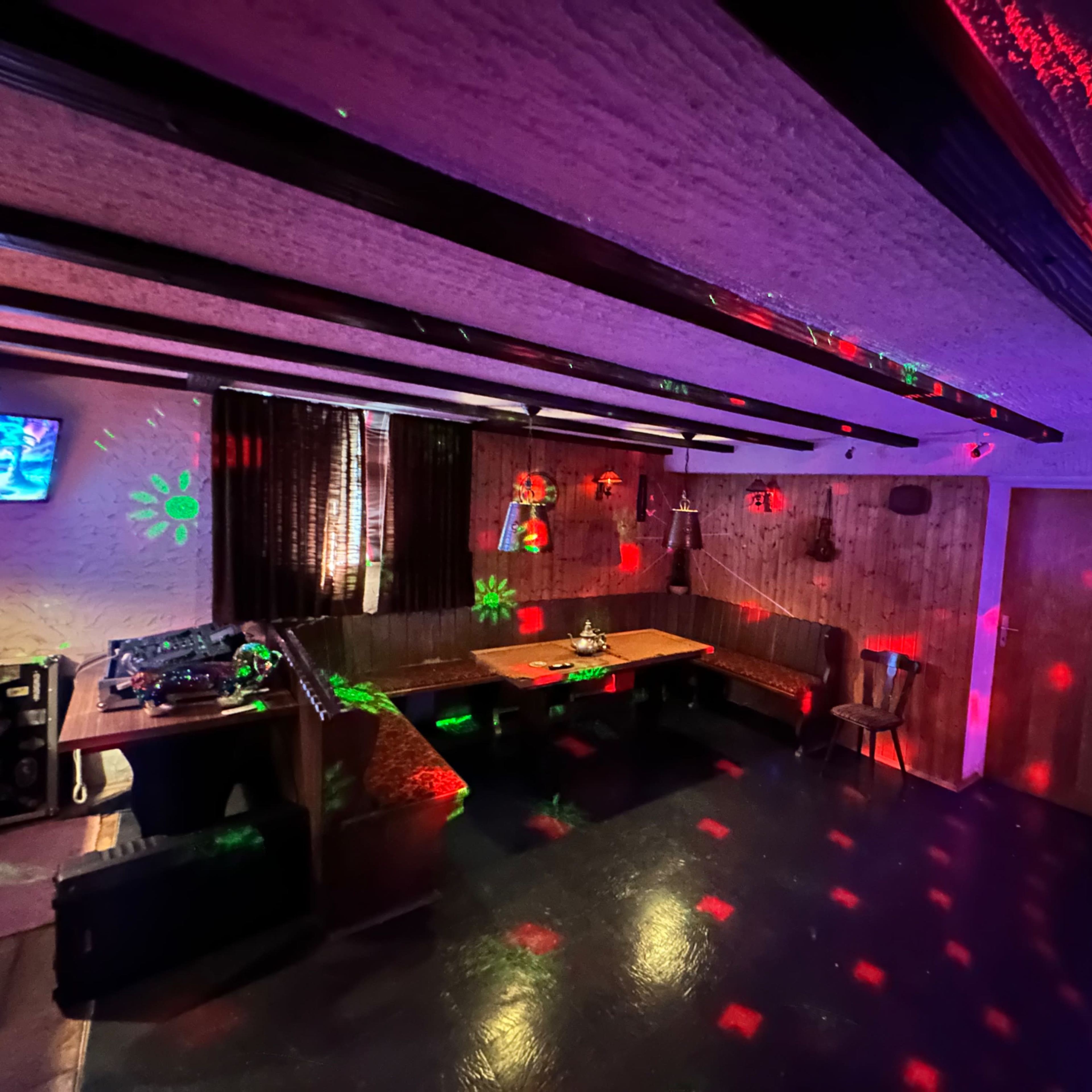 A dimly lit room with a large table and seating, decorated with colorful light projections on the walls and ceiling.