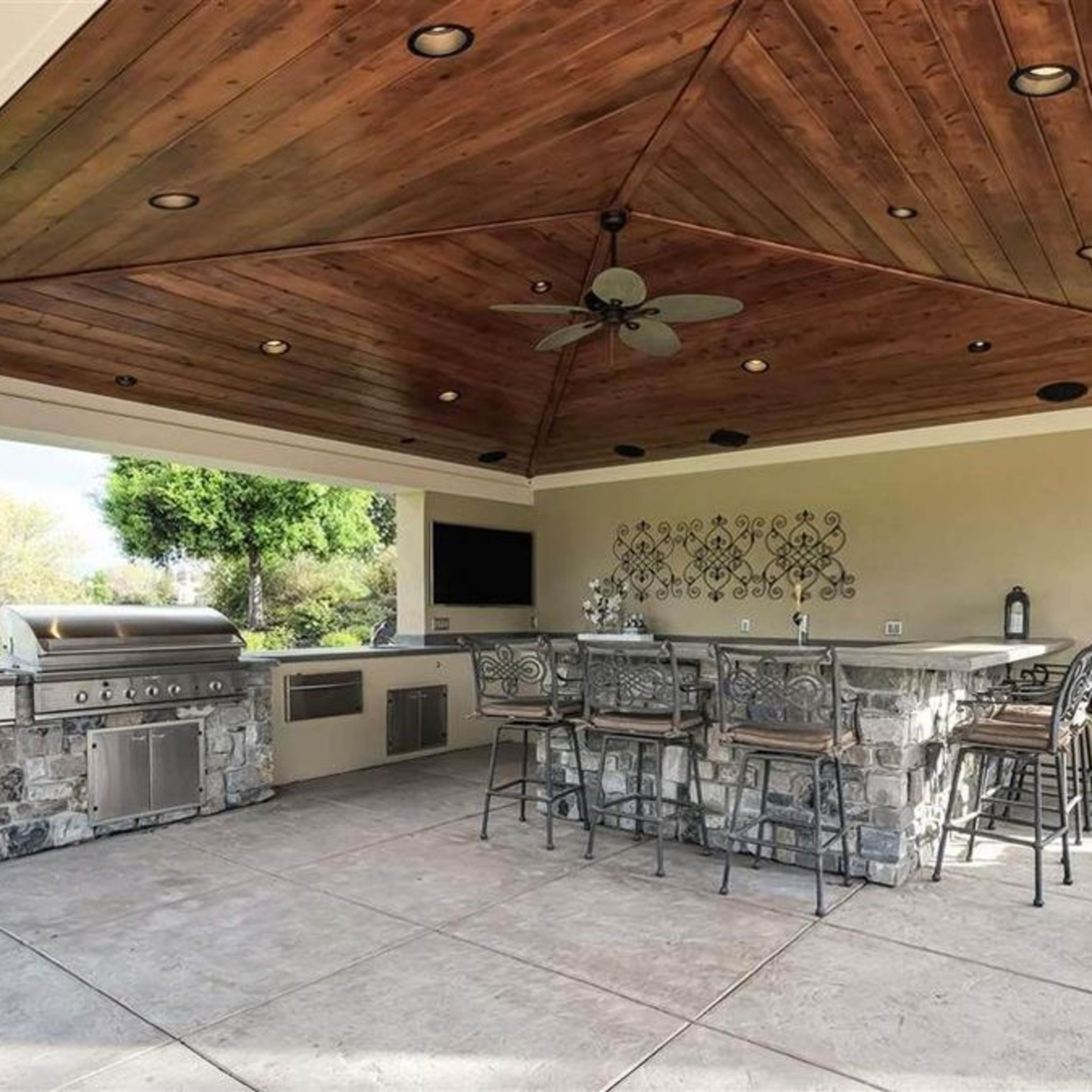 An outdoor kitchen and dining area with a stone grill, bar seating, and a wooden ceiling.