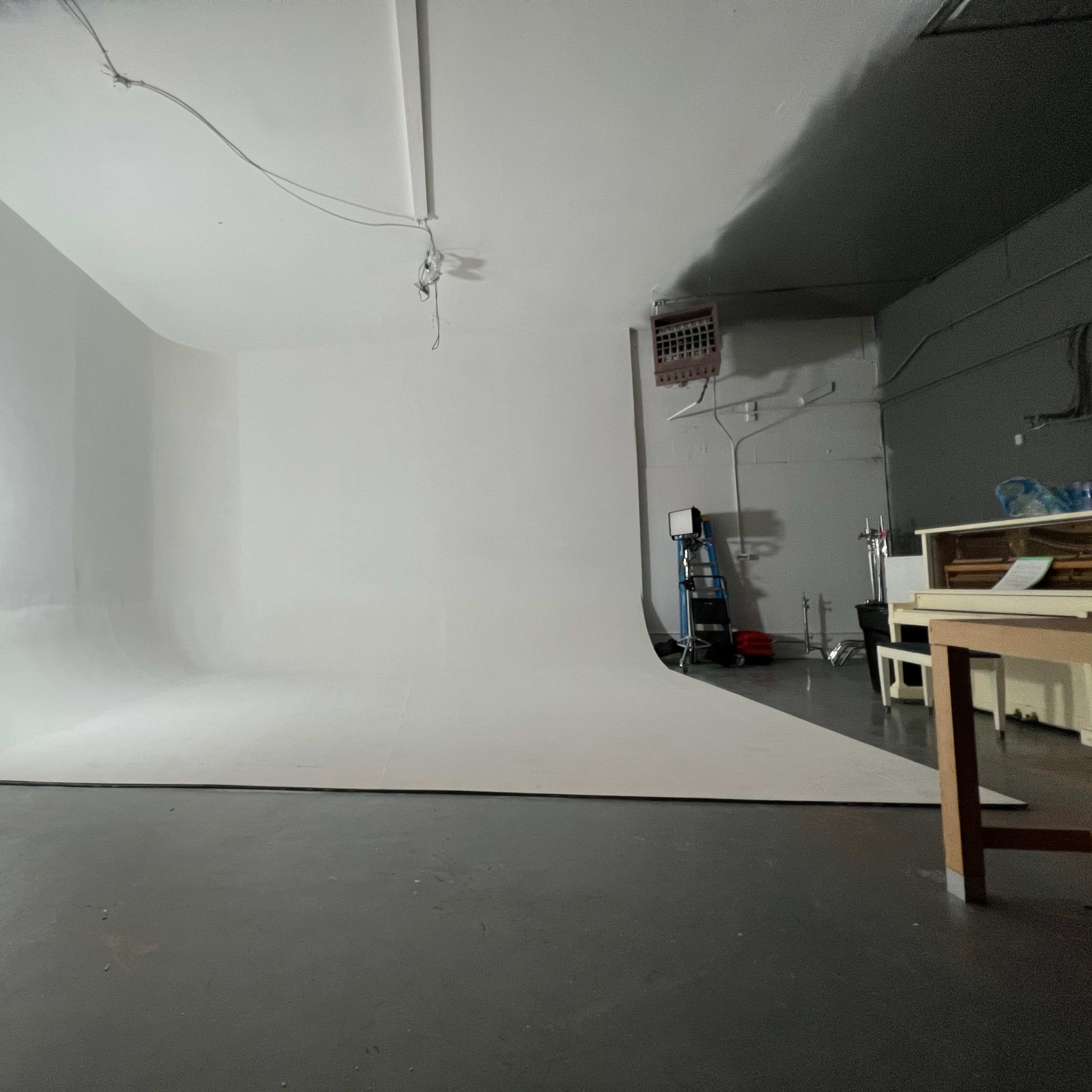 A spacious empty studio with a white backdrop and minimal lighting equipment.