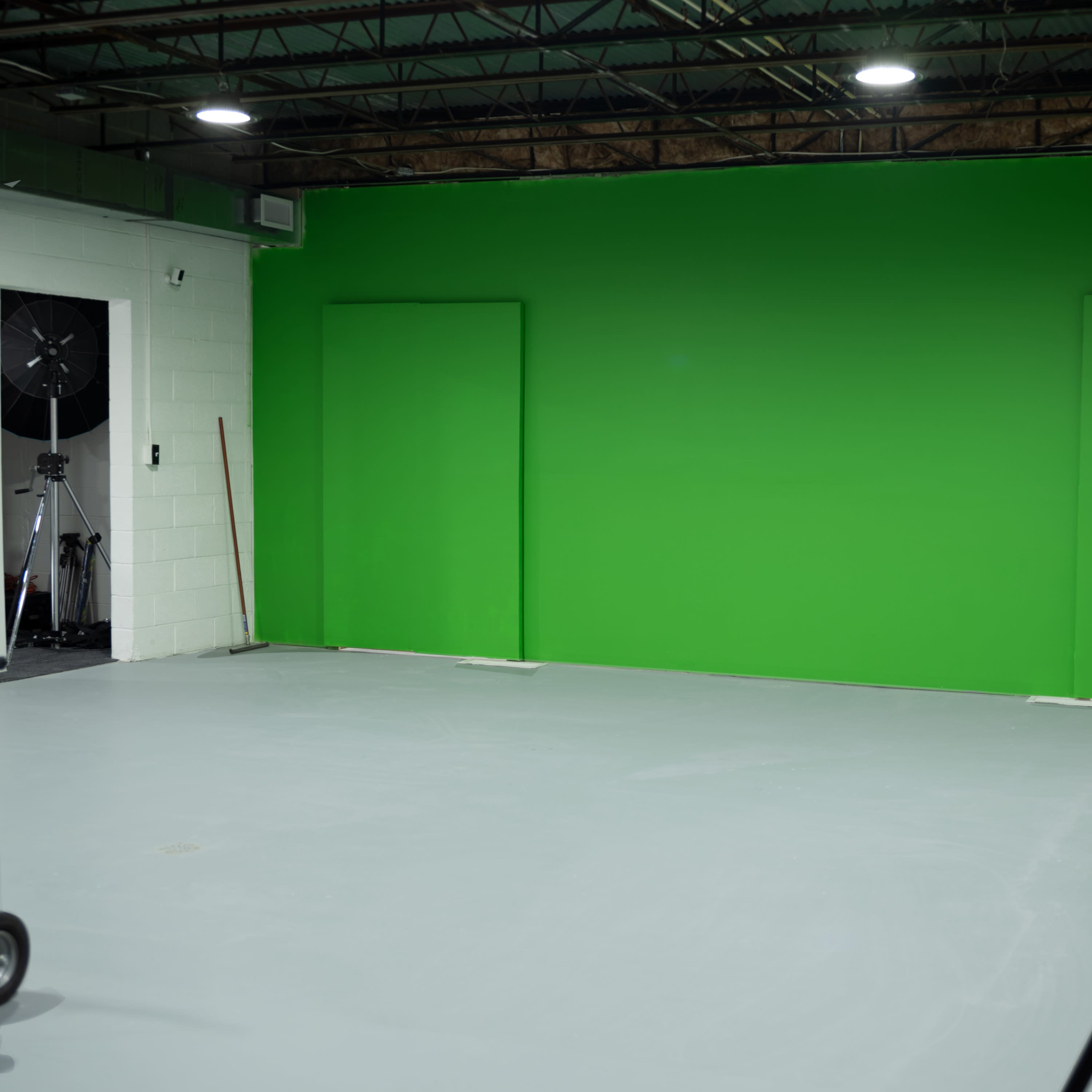 A spacious room with a green screen backdrop, featuring two doorways on the wall.