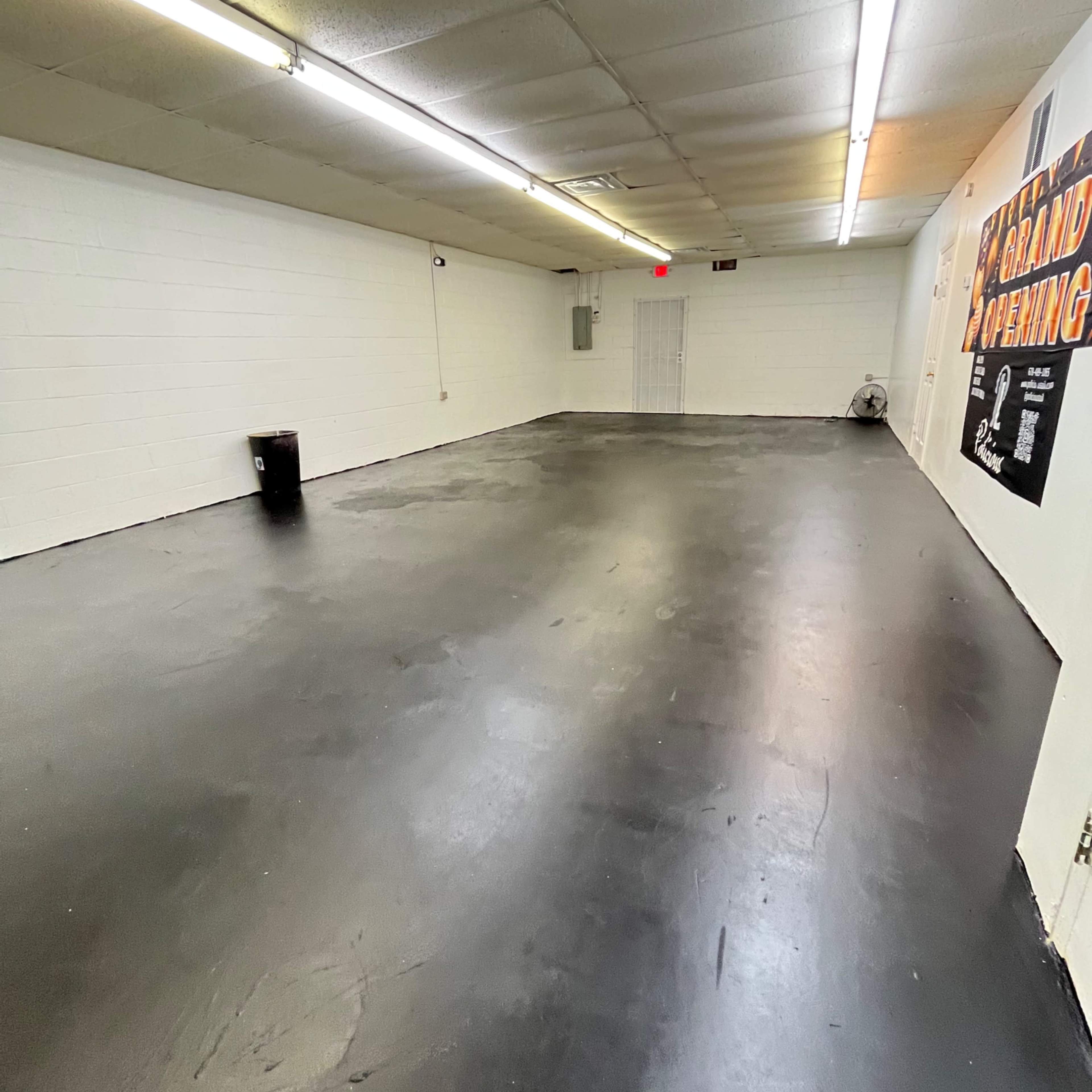 A large, empty room with a black floor, white walls, and overhead fluorescent lighting.
