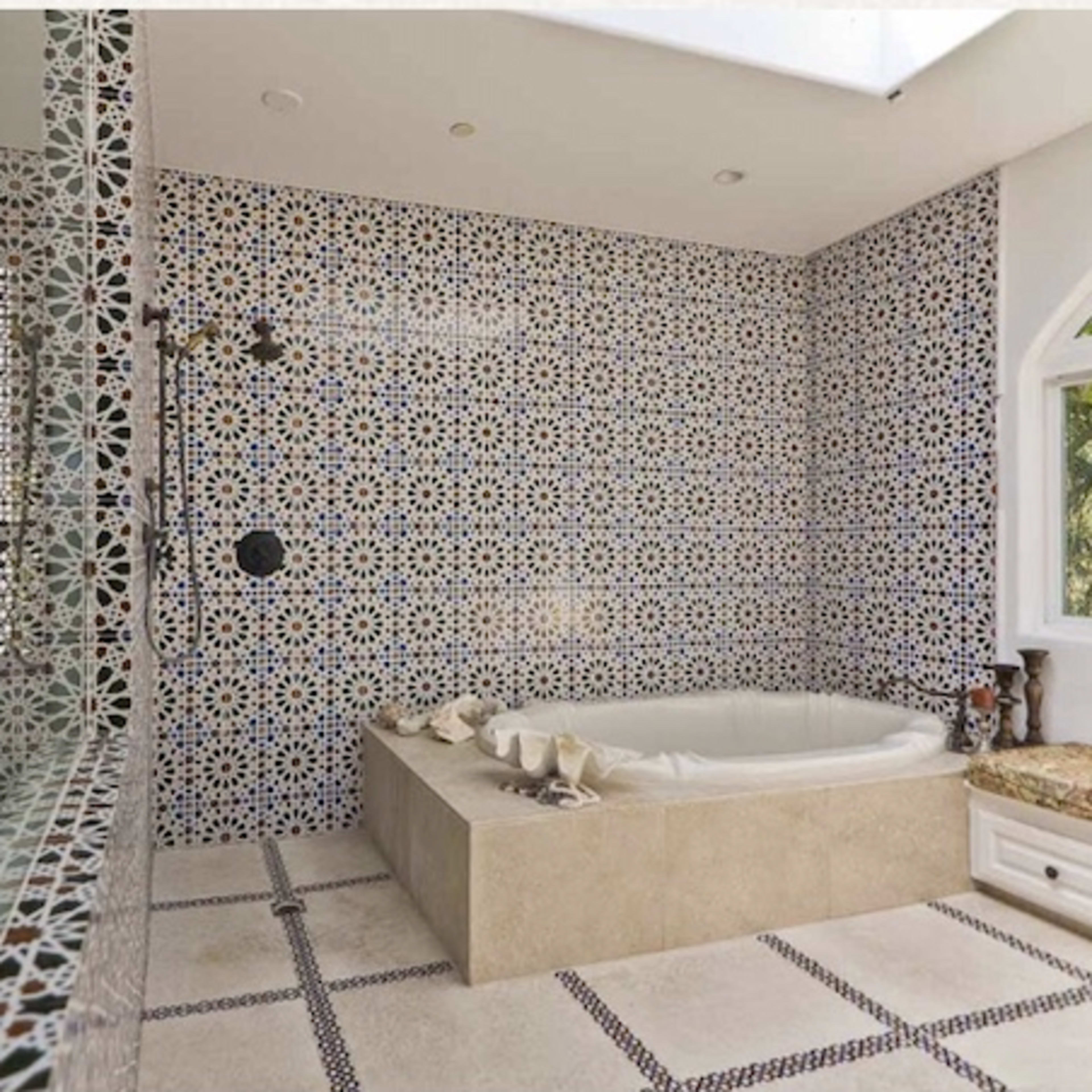 A bathroom featuring intricate patterned tile walls, a large circular bathtub, and a decorative stone counter.