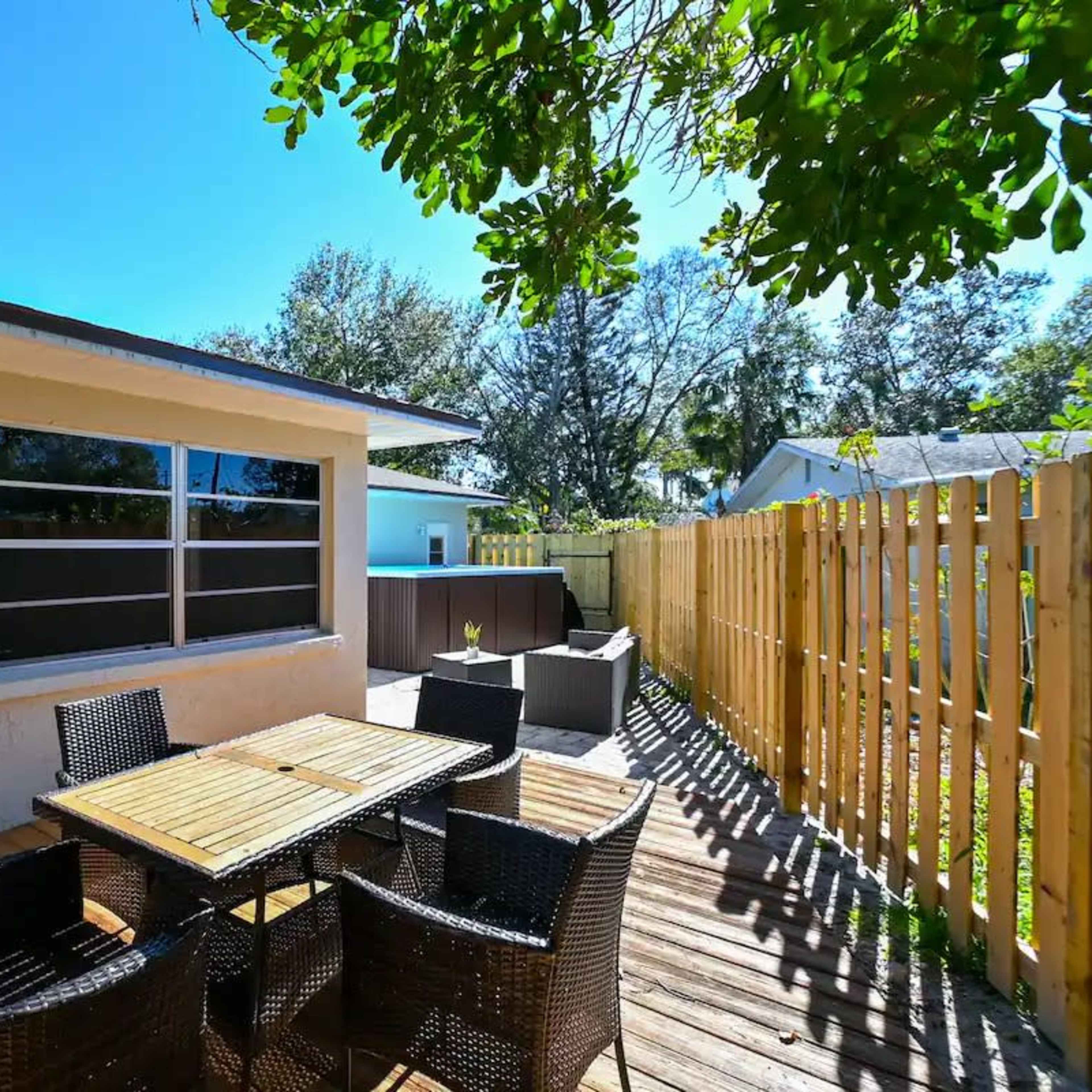 A wooden deck with a table and chairs, bordered by a wooden fence and surrounded by trees.